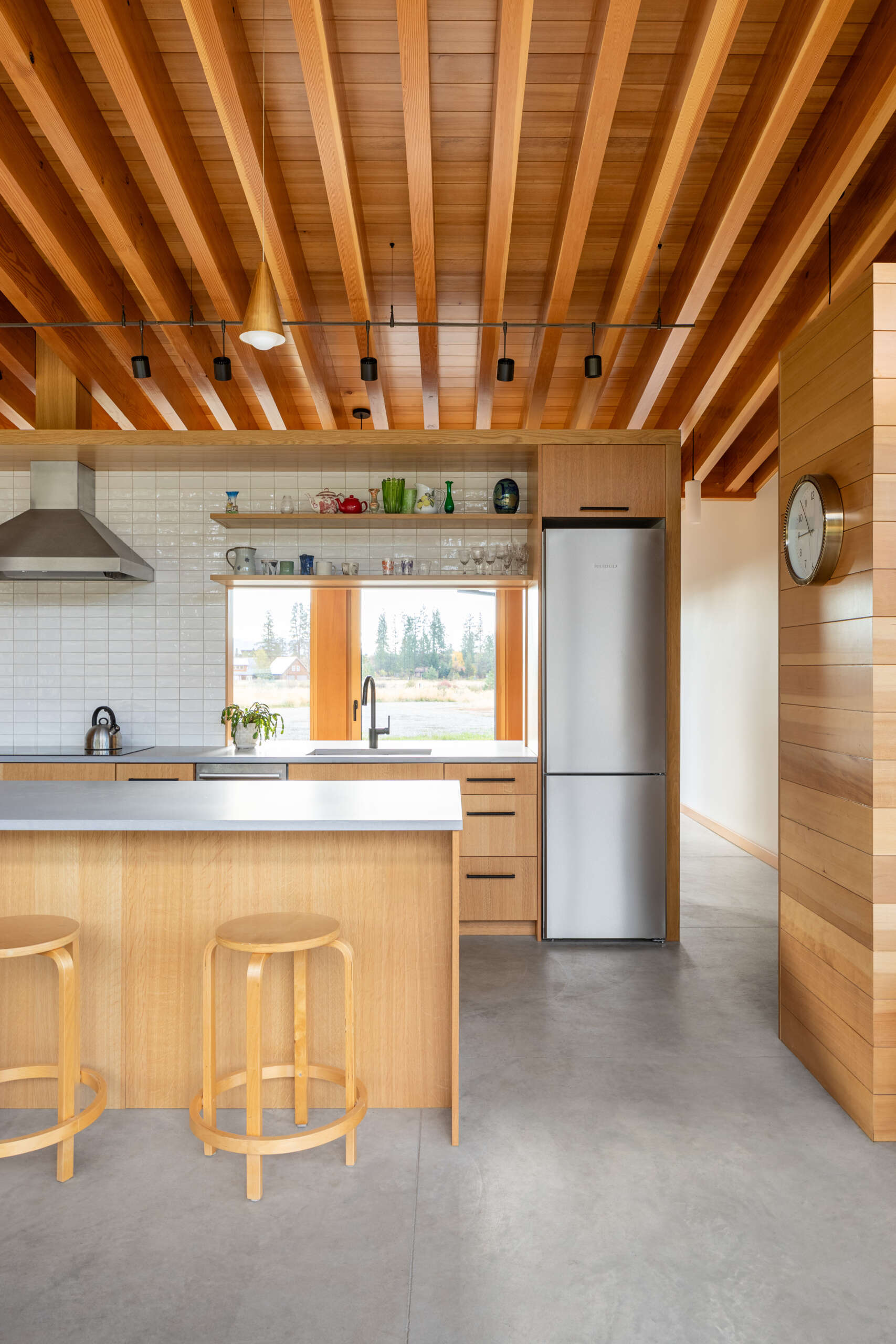 La cocina tiene vistas al prado, haciendo que la naturaleza se sienta parte de la habitación. Un recorte sobre el fregadero brinda visibilidad hacia la entrada, lo que permite a los propietarios ver llegar a los visitantes sin comprometer la sensación de privacidad de la casa.