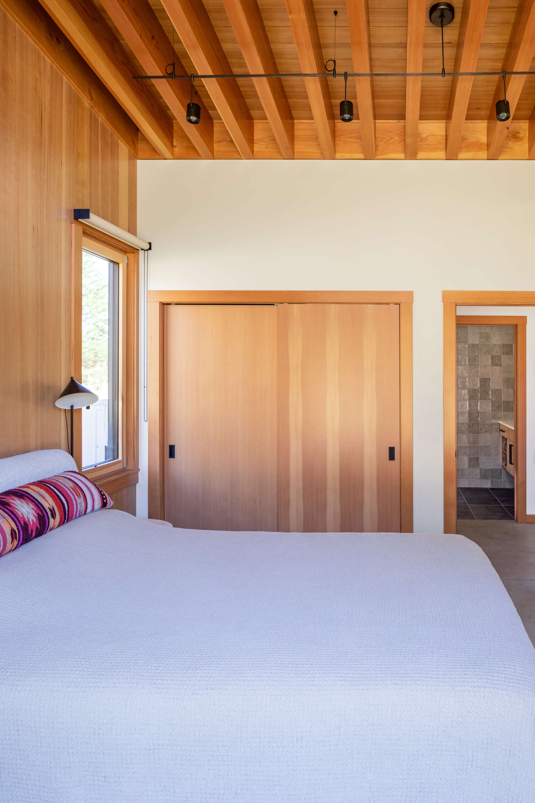 Los dormitorios están construidos alrededor del cielo y el valle. Los grandes ventanales capturan el cielo nocturno, dando la sensación de que el exterior es sólo una parte de la habitación. El baño en suite se mantiene limpio y tranquilo, diseñado para la relajación, con paredes cuadradas de azulejos grises y un tocador de madera flotante.