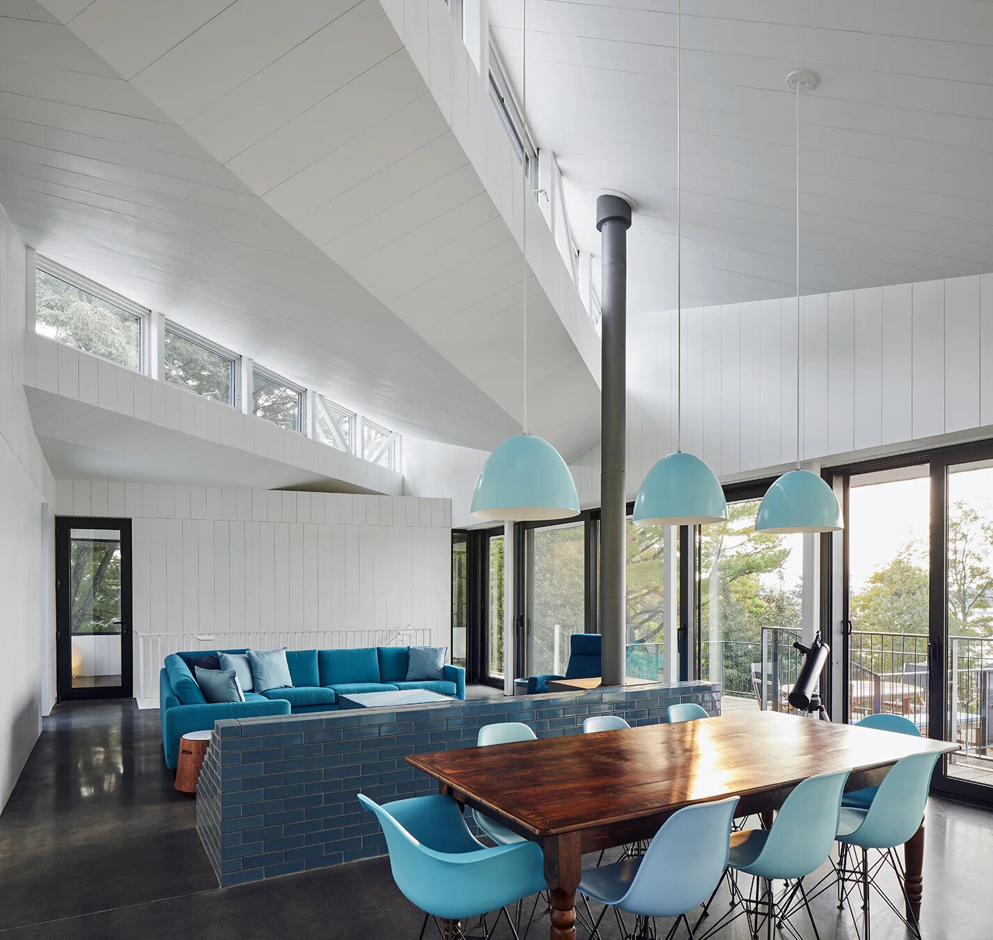 Inside Sky House, bright white walls meet polished concrete floors and turquoise accents. The open plan living area centers around a vivid blue brick surround that creates both warmth and color.