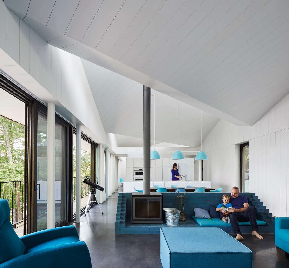 Inside Sky House, bright white walls meet polished concrete floors and turquoise accents. The open plan living area centers around a vivid blue brick surround that creates both warmth and color.