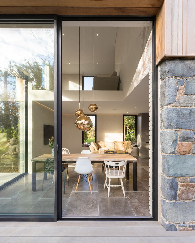 This modern home is wrapped in Guernsey granite, cedar cladding, and a living wall with 13 native species that soften the structure and blend it into the forested setting.