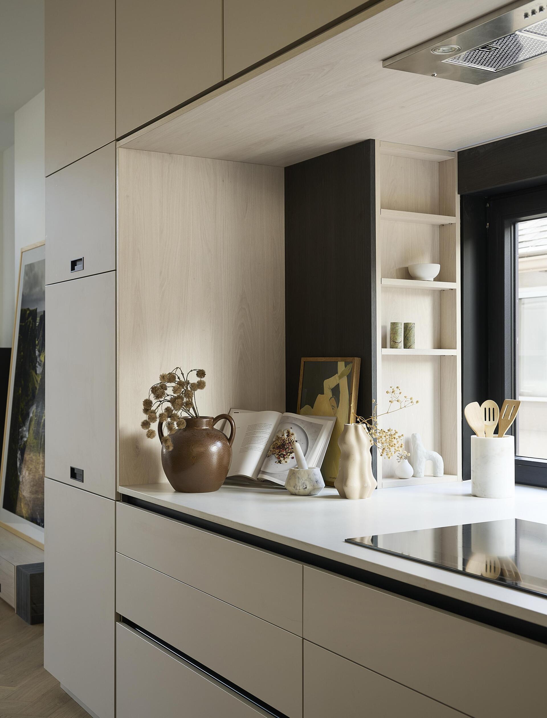 At the centre of this modern home, the kitchen sits against the stairwell. A large island in concrete toned Caesarstone pairs with light grey and whitewashed oak cabinetry trimmed in black. The island’s red toned brick end gables add gentle warmth. A full width window replaces a traditional backsplash, pulling natural light and surprising depth into the room.