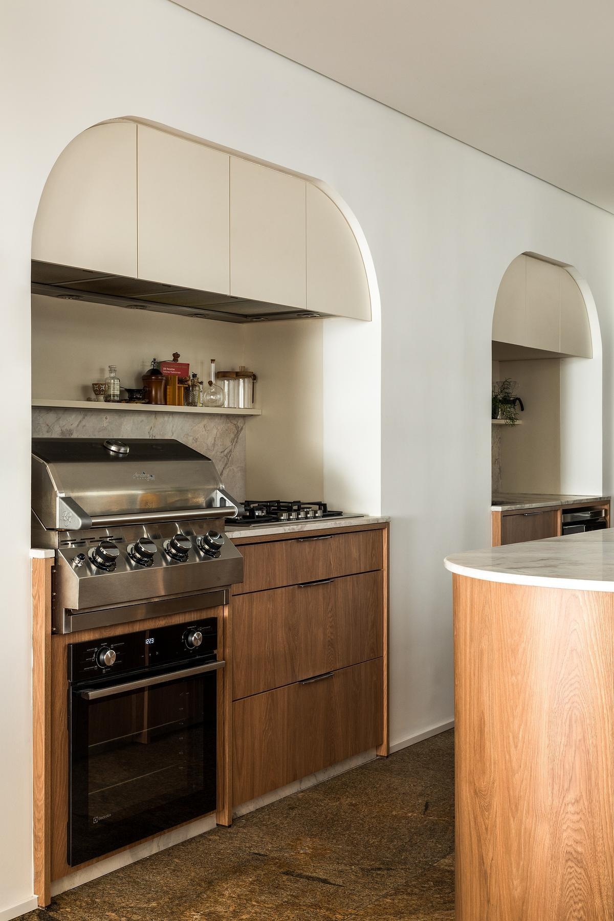 One of the homeowners’ biggest wishes was to make the kitchen the social heart of the apartment. Previously enclosed, it was opened to brighten circulation and connect it to daily life. A central island now anchors the space, paired with the Helga Bar Stool by Estudio Bola and the Wrap Lamp by Jader Almeida. Even appliances like the Char Broiler blend into the layout, keeping the look calm and unified.