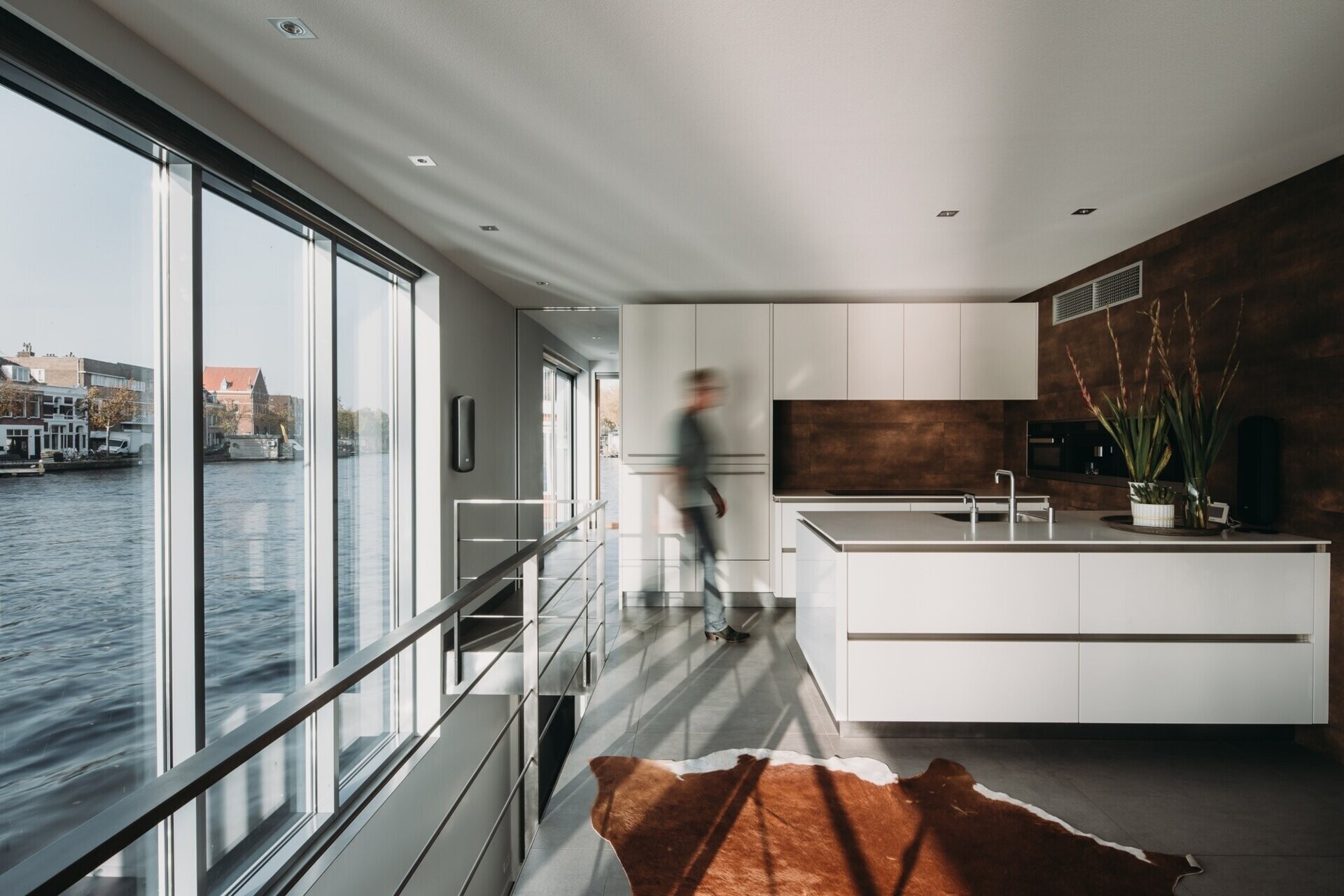 La cocina minimalista cuenta con gabinetes blancos y encimeras a juego, con vista directa al río y luz natural.
