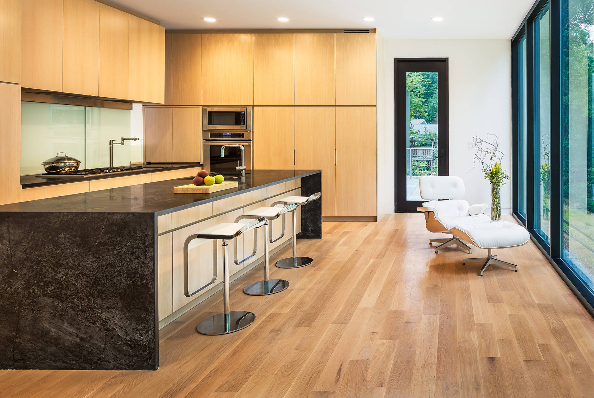 Soft wood tones meet dark stone and a wall of windows in the kitchen at Bridge House, where nature sets the mood.