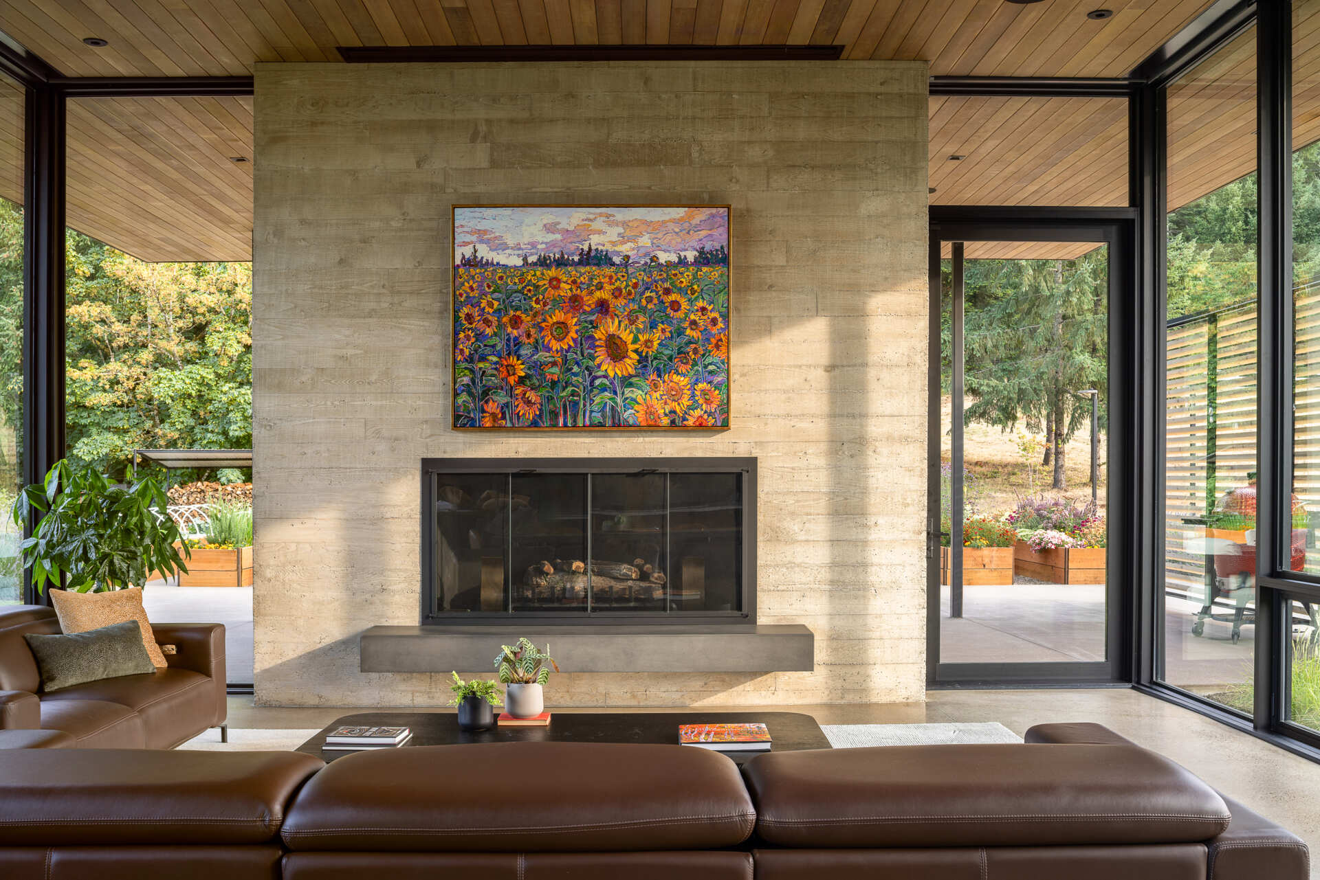 The great room unfolds under twelve foot ceilings and three walls of glass. Concrete floors and a cedar ceiling run uninterrupted from inside to outside, adding to the indoor outdoor feel. A board formed concrete fireplace grounds one end of the space, while the open plan keeps the kitchen, dining, and living areas visually connected. 