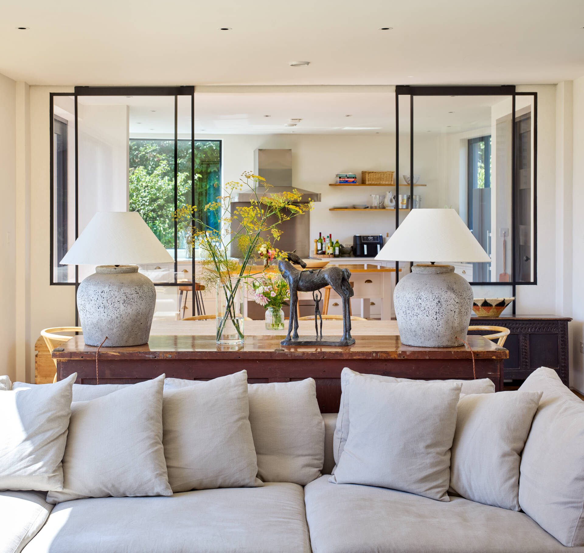 Large windows in the open living room frame the meadow. Light becomes part of the experience in every season. The interior materials keep the feeling grounded and warm, with natural tones echoing the surroundings.