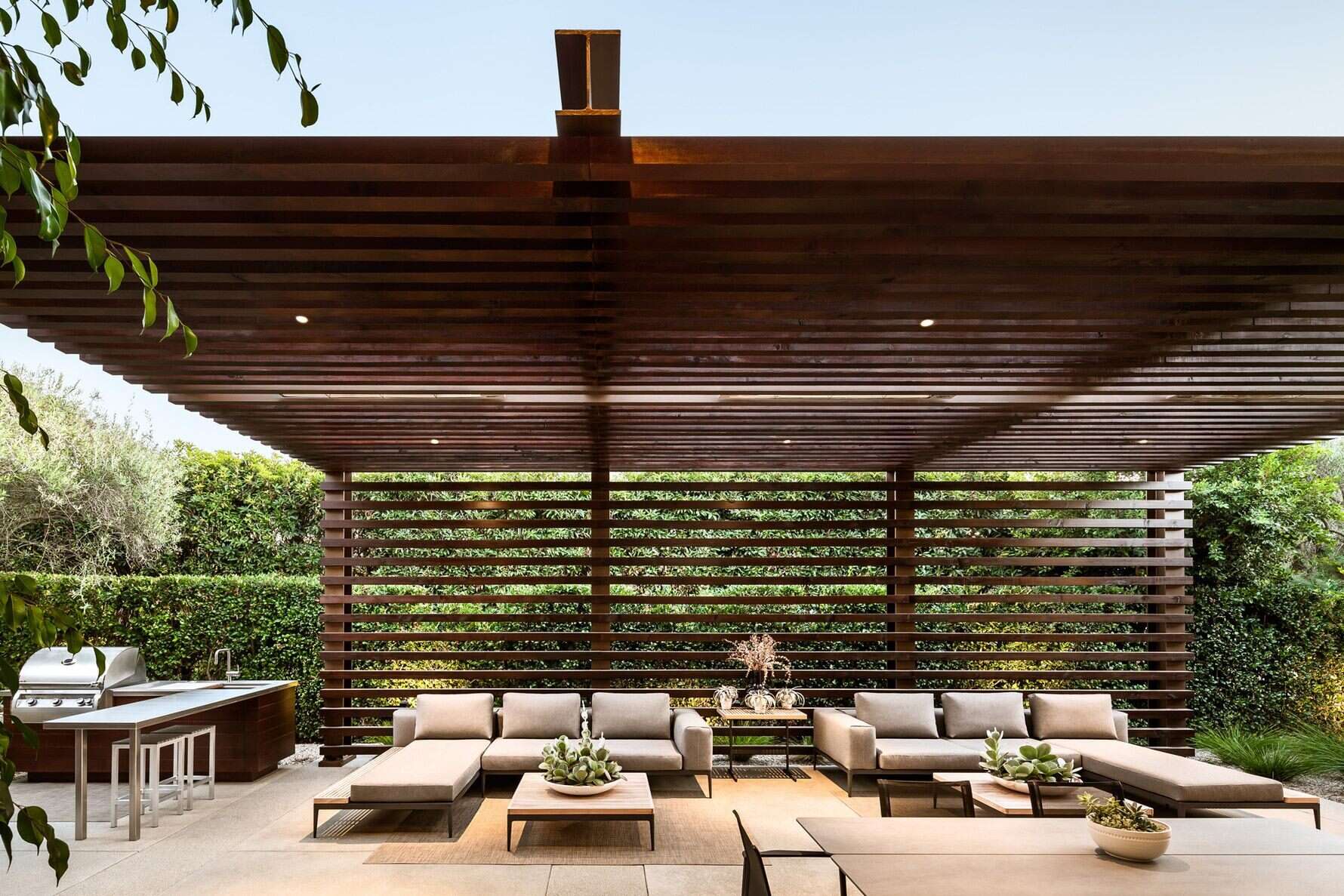 A pergola-topped outdoor lounge with fireplace and BBQ blends relaxation and California elegance.