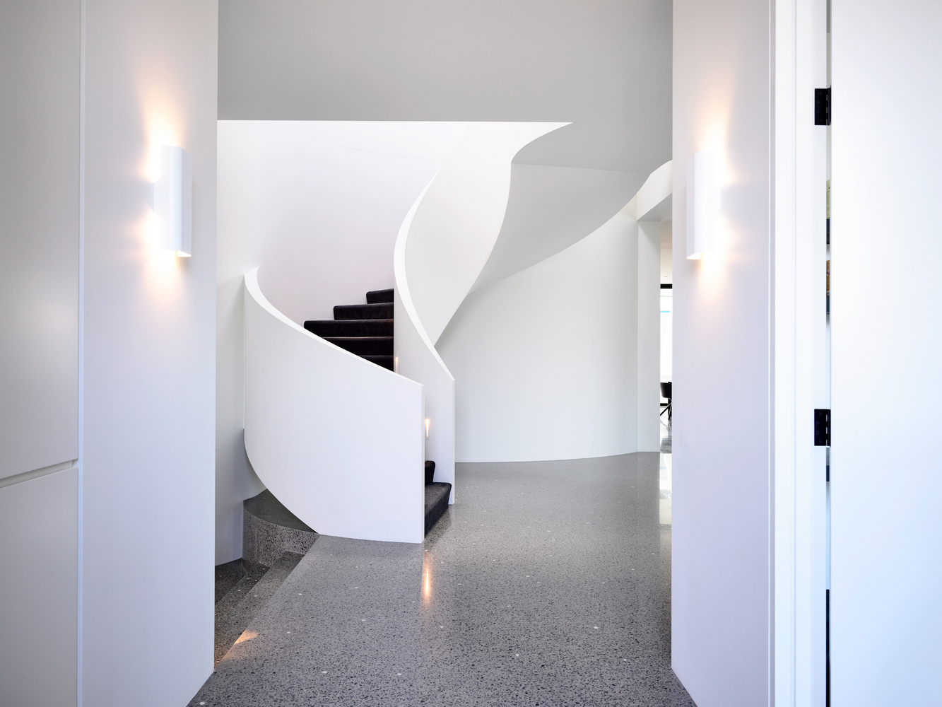 Custom spiral stairs with black treads and a circular skylight above create a sculptural moment inside the home.
