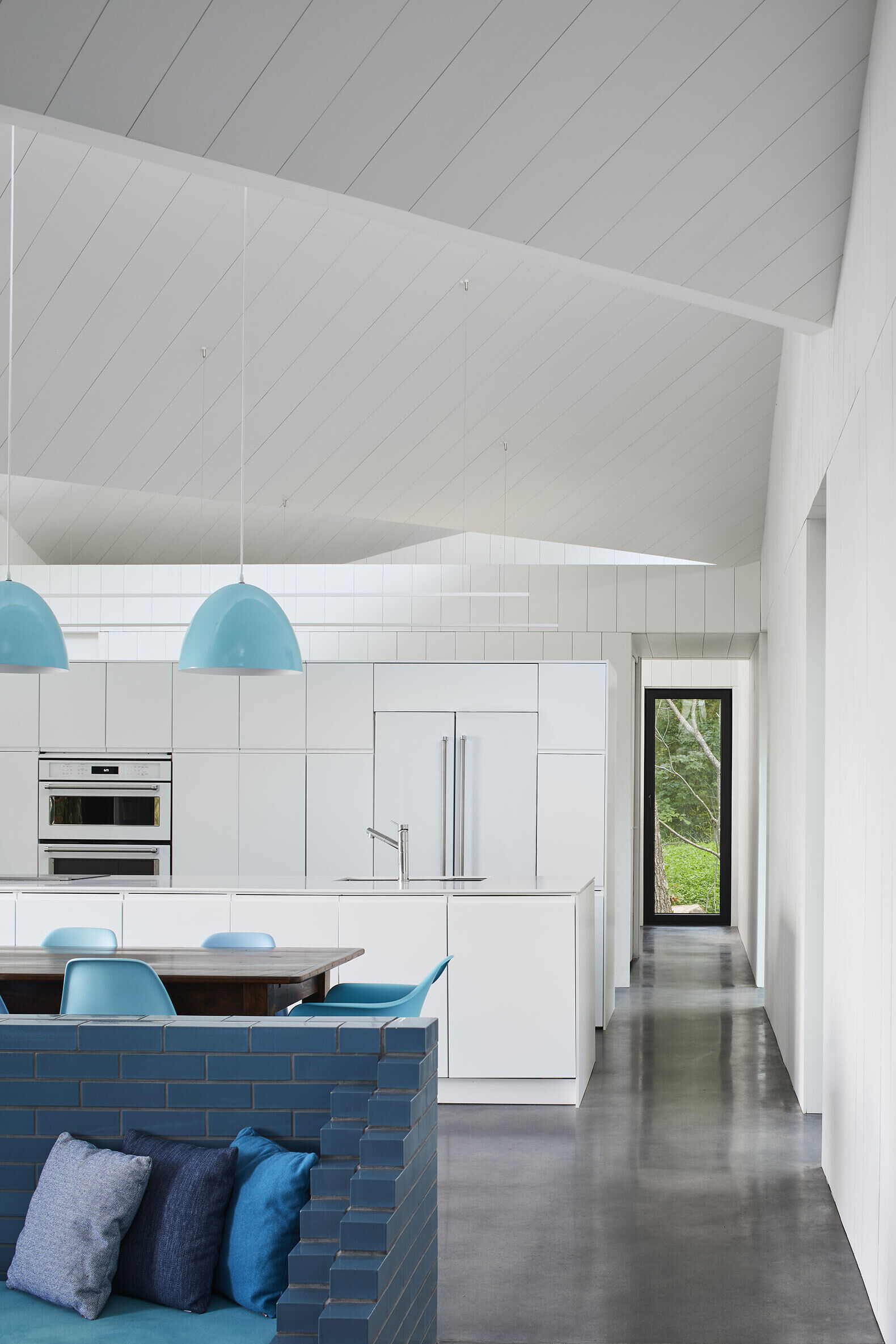 Inside Sky House, bright white walls meet polished concrete floors and turquoise accents. The open plan living area centers around a vivid blue brick surround that creates both warmth and color.