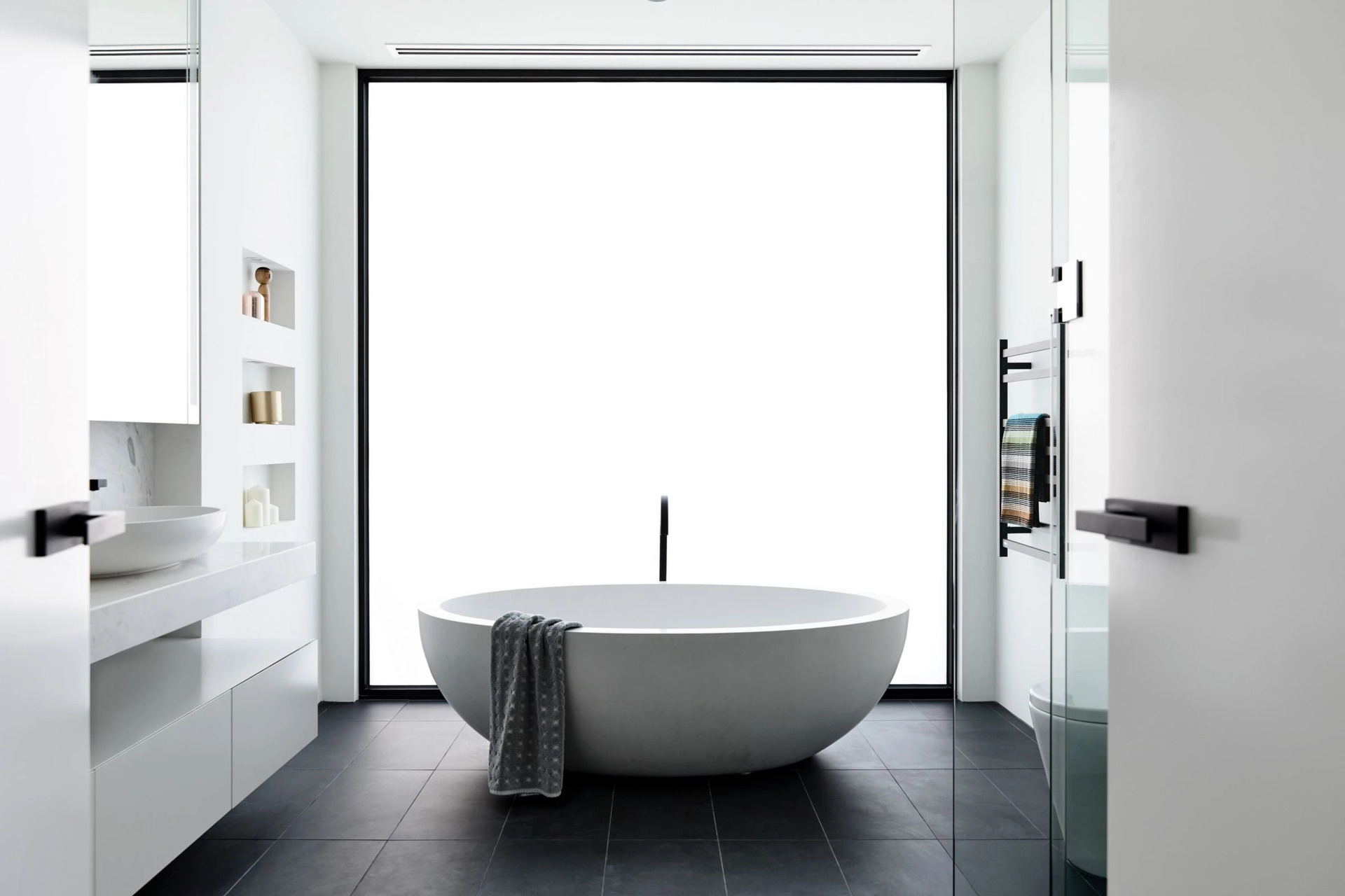 A minimalist bathroom with a frosted window behind the freestanding bathtub that keeps the space full of natural light.