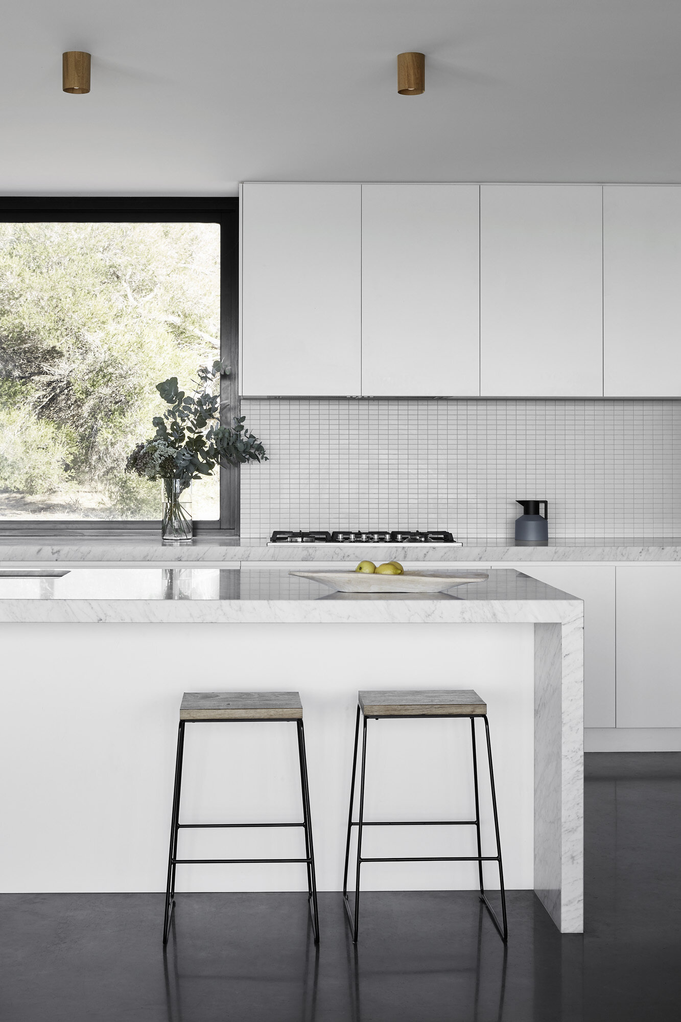Minimalist white cabinetry in the kitchen is paired with exposed wood shelving, creating a clean look that stands out against the dark window frames and flooring.