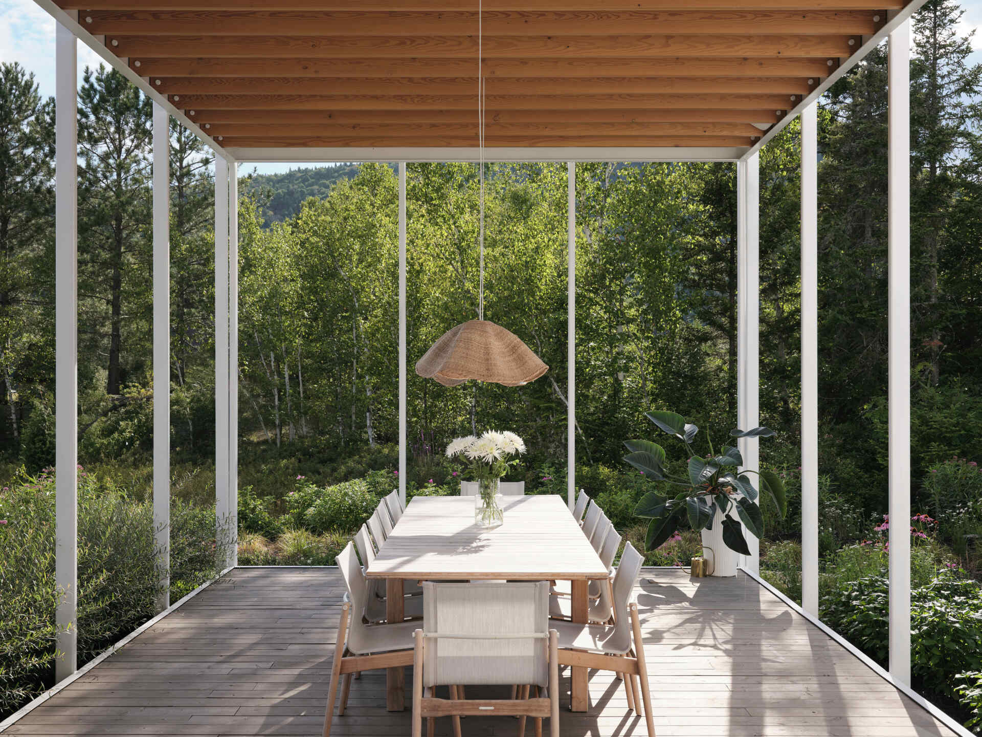 A large veranda extends outward beneath a wood pergola, becoming the ideal place for outdoor dining.