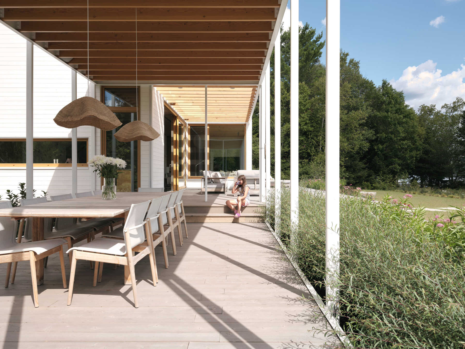 A large veranda extends outward beneath a wood pergola, becoming the ideal place for outdoor dining.
