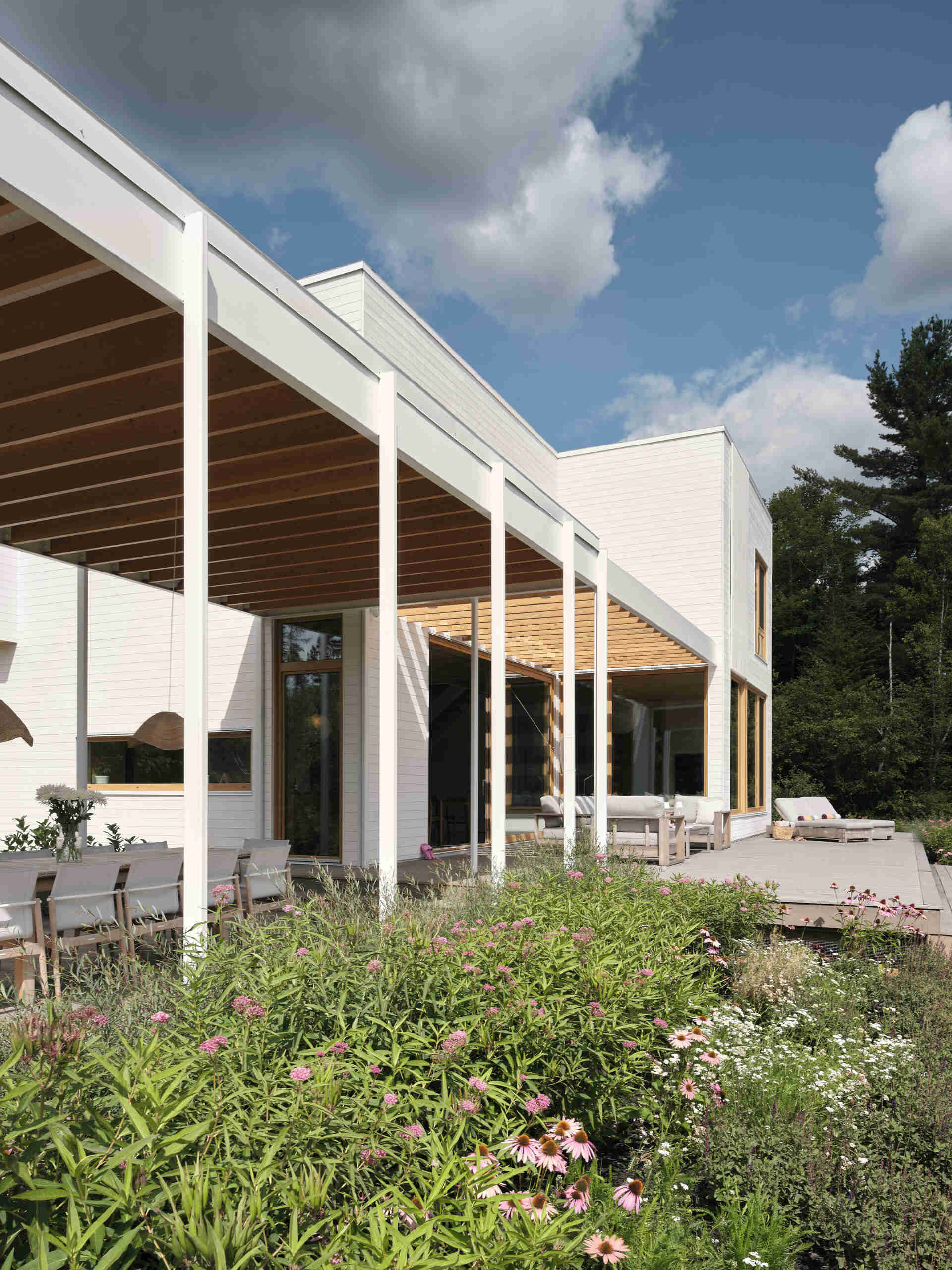 A large veranda extends outward beneath a wood pergola, becoming the ideal place for outdoor dining.