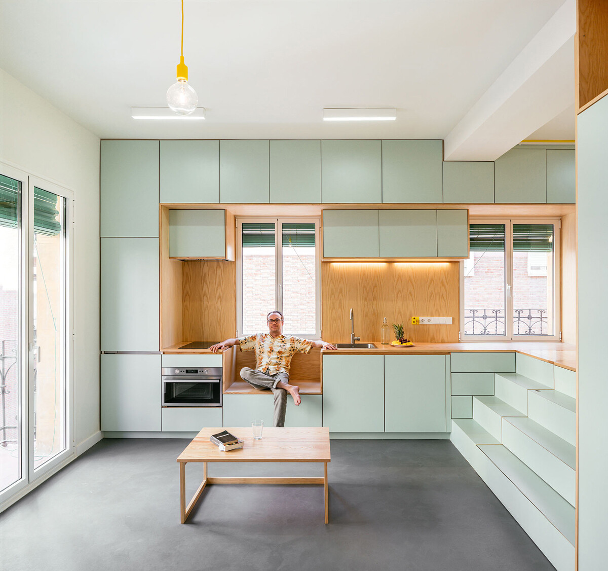 Soft green cabinets and warm wood details shape a simple, bright kitchen that blends into the open living space.