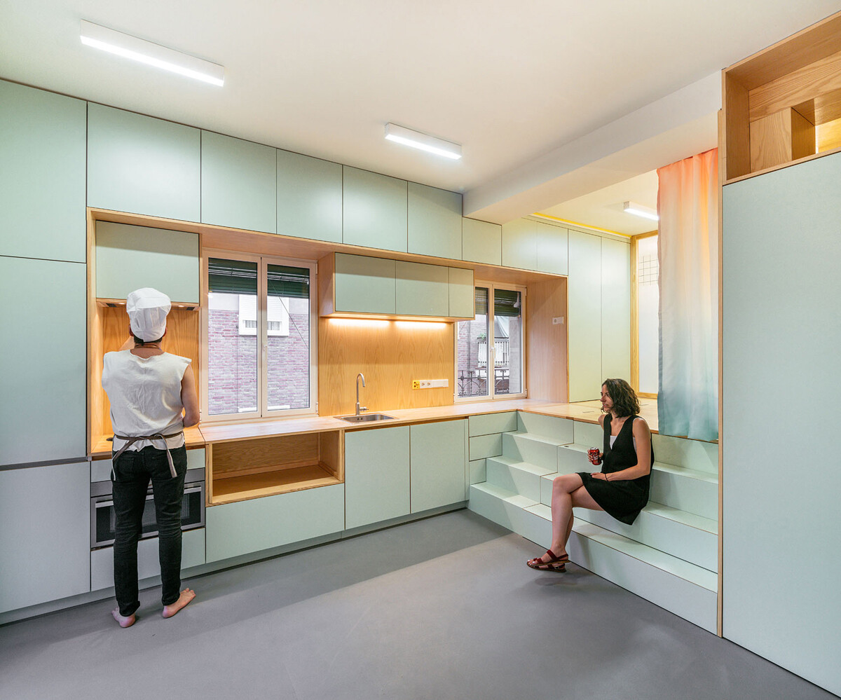 Soft green cabinets and warm wood details shape a simple, bright kitchen that blends into the open living space.