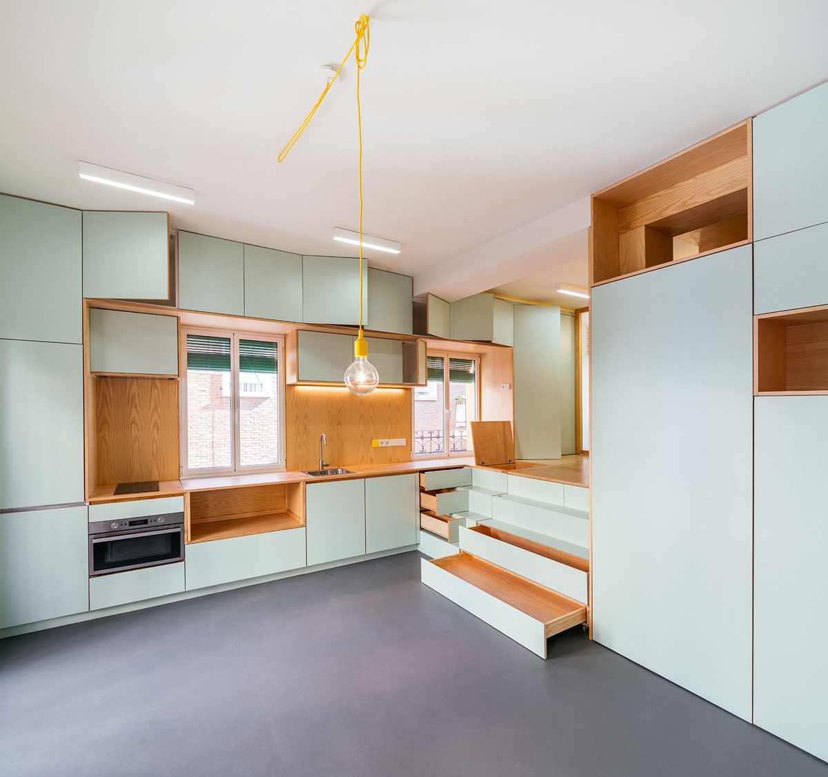 Stair like storage modules lead to a cosy raised bedroom framed by a colourful curtain and warm wood shelving.