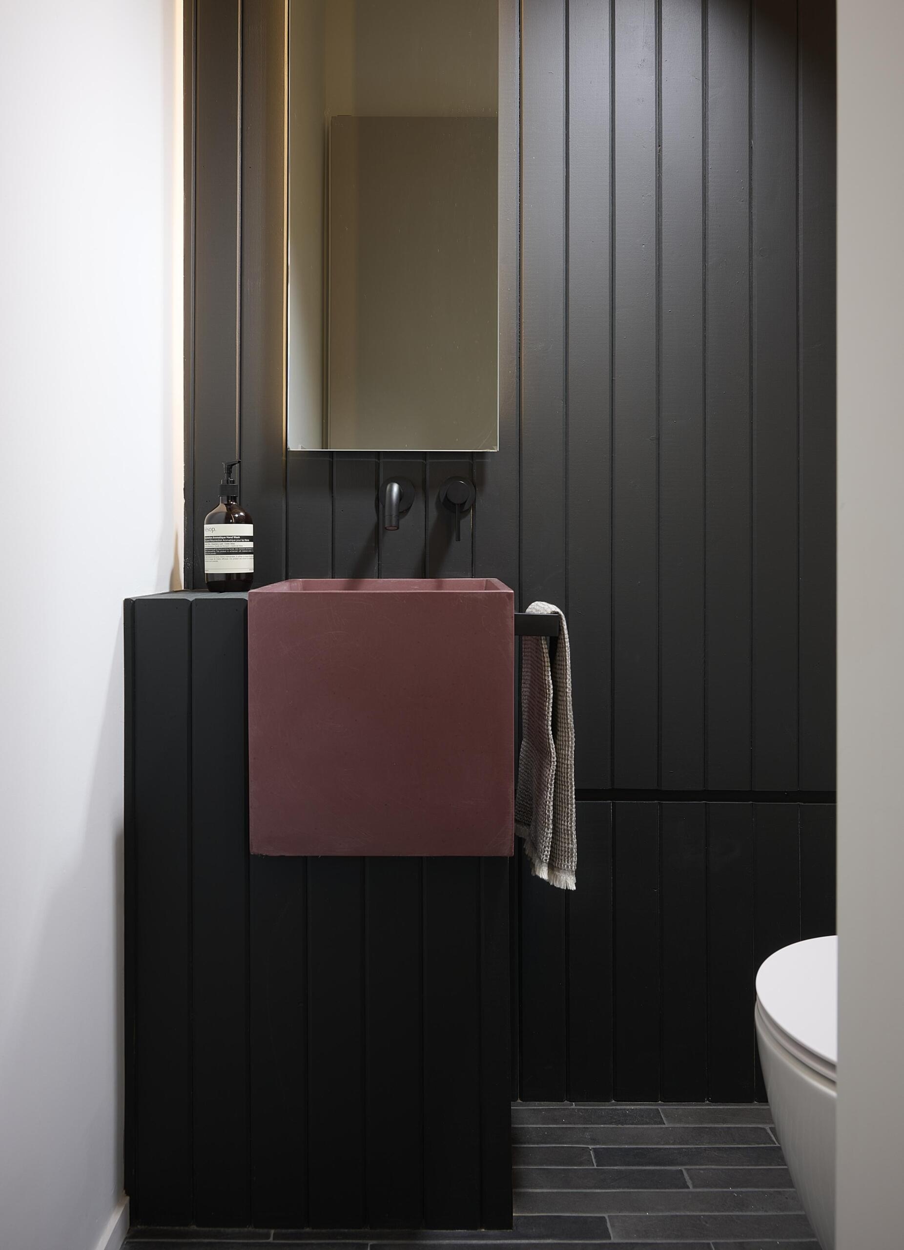 This powder room has a black accent wall and slim black brick underfoot sets a grounding base.