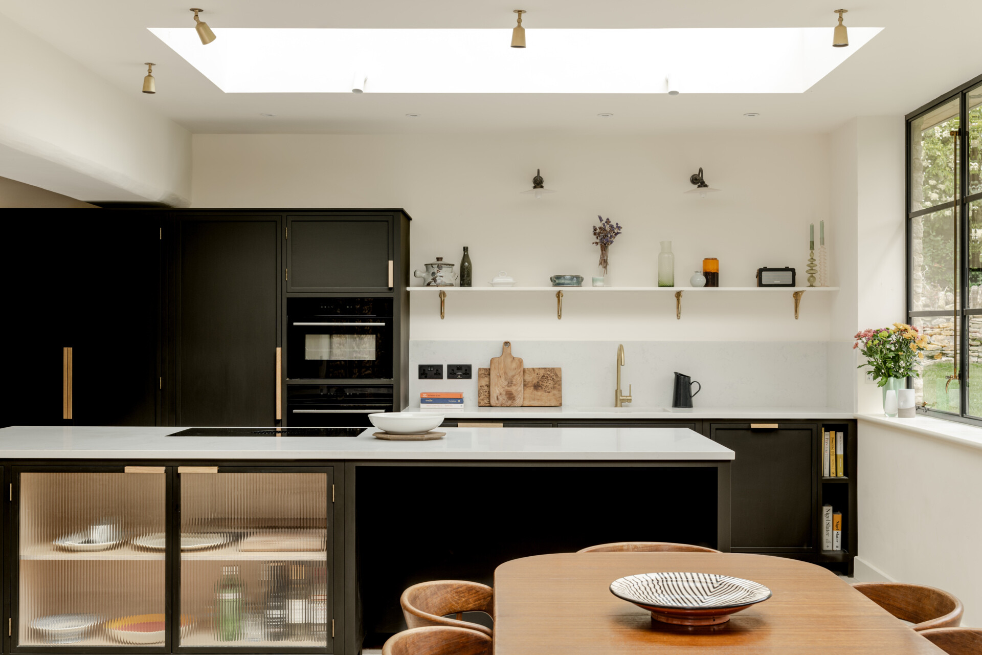 The kitchen sits within the open plan arrangement, using the new glazing and steel details to add clarity and simplicity while keeping the palette restrained. The dark kitchen cabinets complement the window frames and offer contrast to the light interior, while a skylight adds natural light.