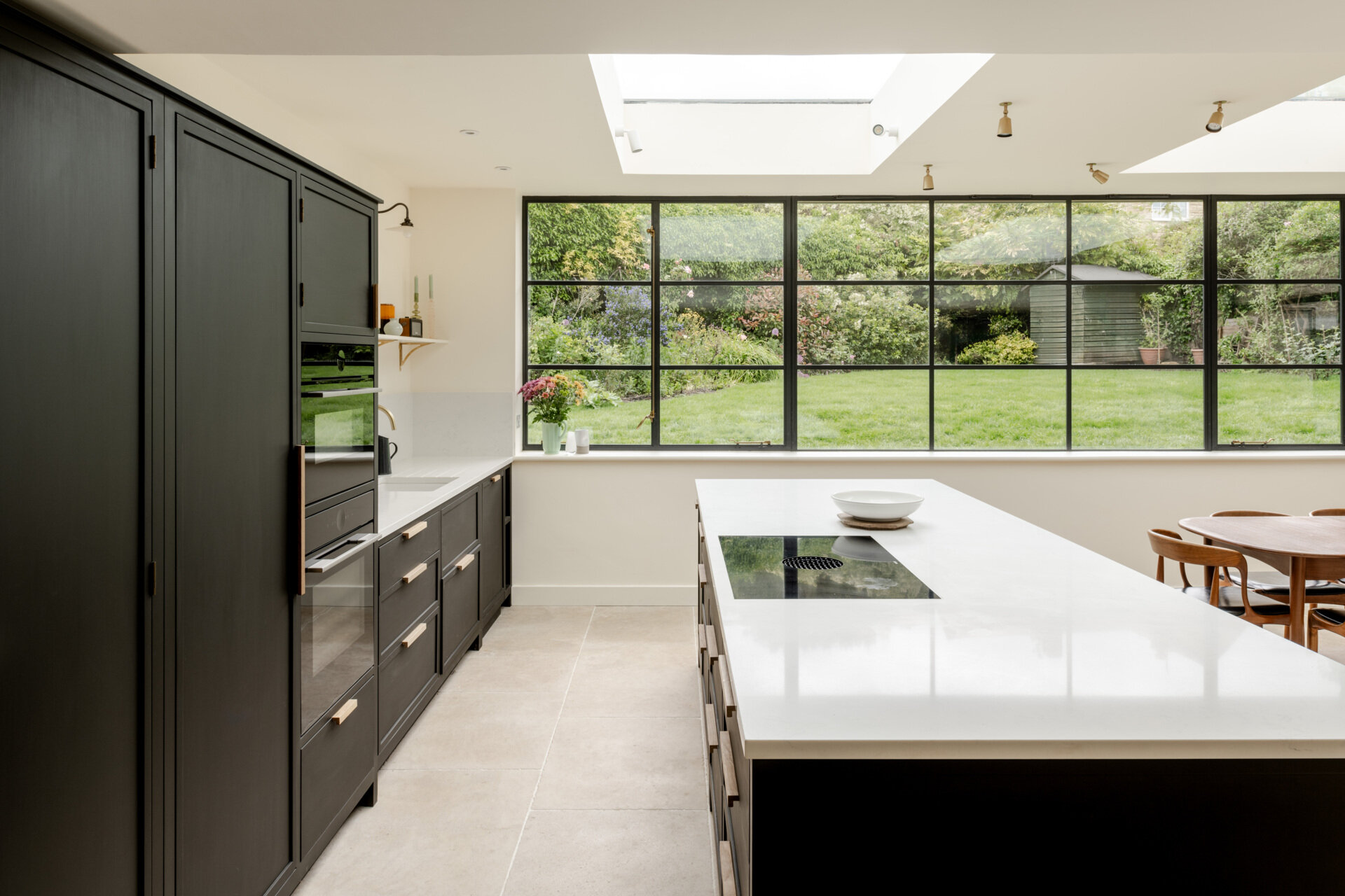 The kitchen sits within the open plan arrangement, using the new glazing and steel details to add clarity and simplicity while keeping the palette restrained. The dark kitchen cabinets complement the window frames and offer contrast to the light interior, while a skylight adds natural light.