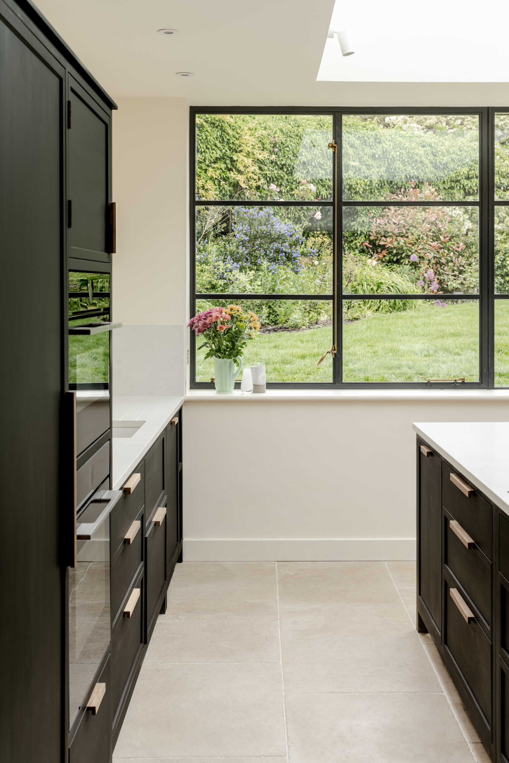 The kitchen sits within the open plan arrangement, using the new glazing and steel details to add clarity and simplicity while keeping the palette restrained. The dark kitchen cabinets complement the window frames and offer contrast to the light interior, while a skylight adds natural light.