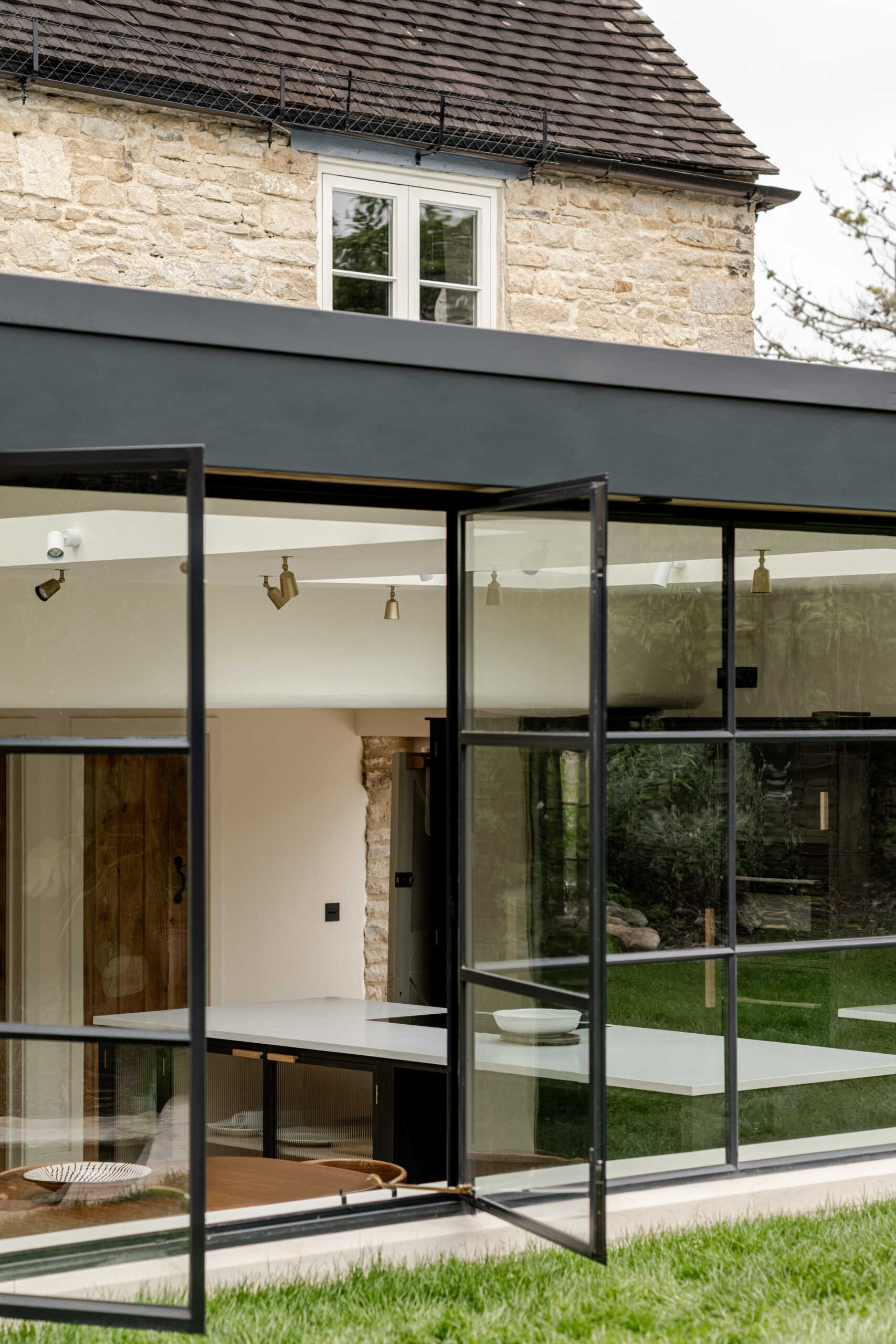 The extension sits at the rear as a low, single storey volume. By sinking it slightly into the garden, its profile stays subtle, reducing its visibility to neighbours and protecting views within the Charlbury Conservation Area. Slim steel framing, large glazing, and Cotswold stone create a gentle dialogue between old and new.