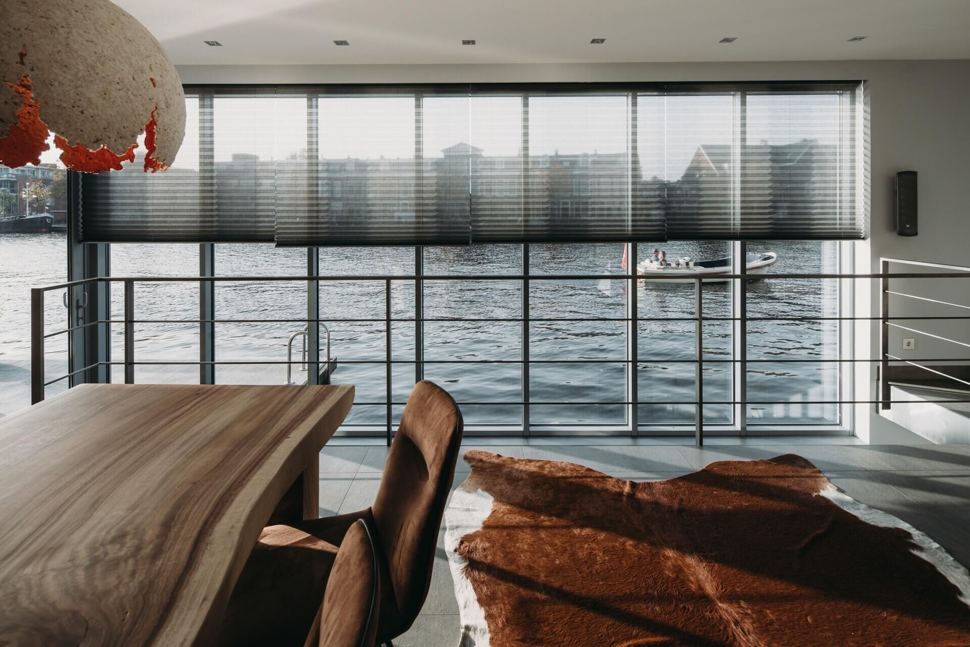 El acogedor comedor cuenta con mesas de madera, colgantes esculturales y ventanas de pared a pared con vista al río.