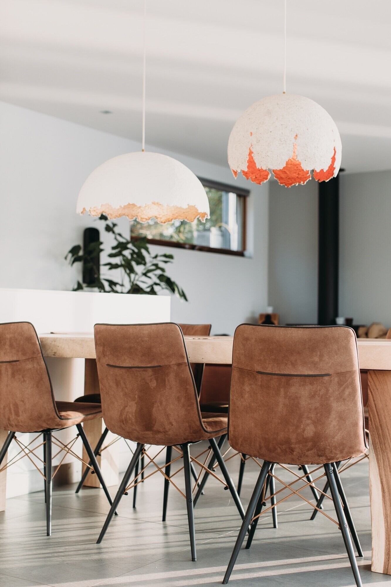 El acogedor comedor cuenta con mesas de madera, colgantes esculturales y ventanas de pared a pared con vista al río.