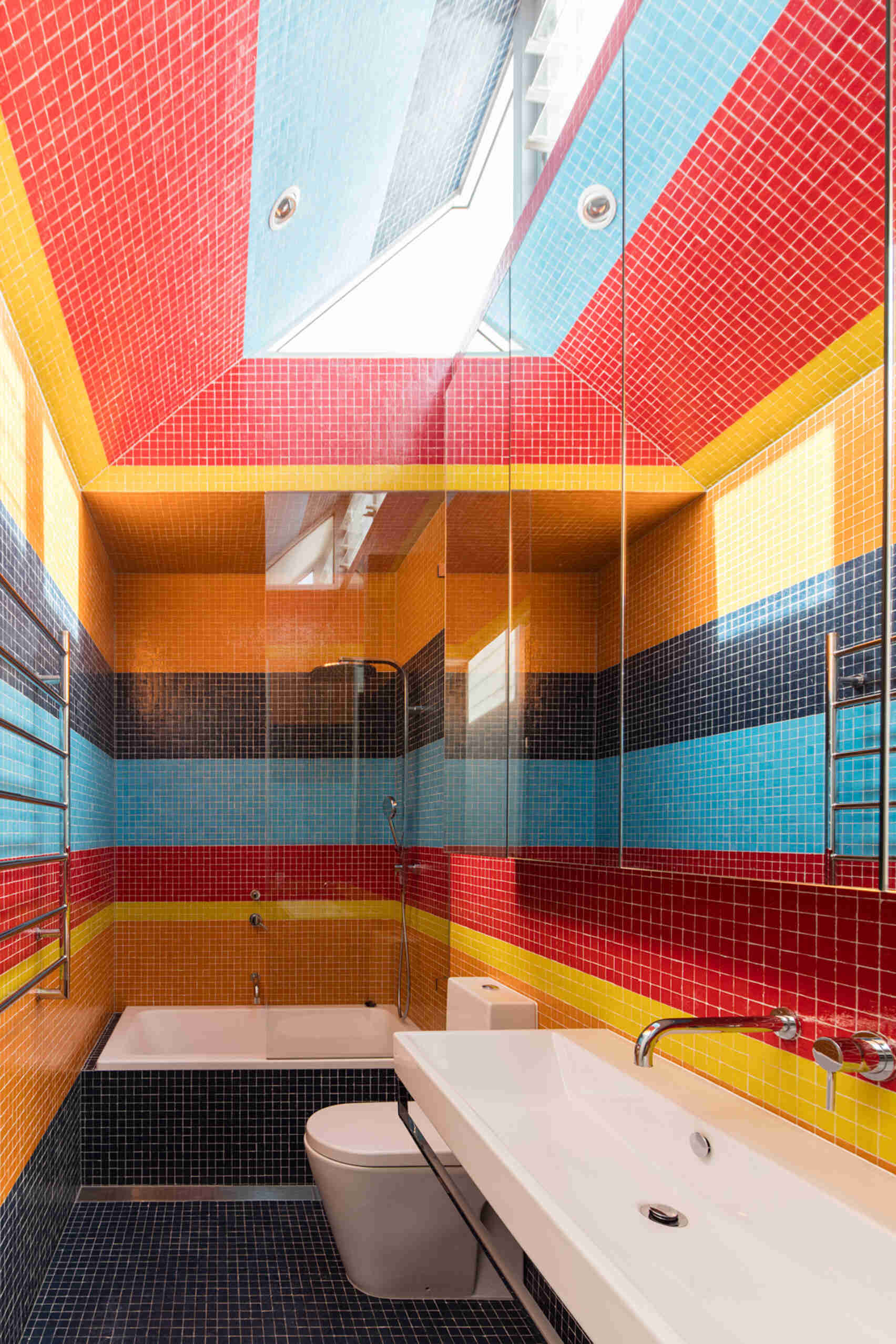 Bright tiles in bold stripes run across the floor, climb the walls, and continue over the ceiling in this modern bathroom. 