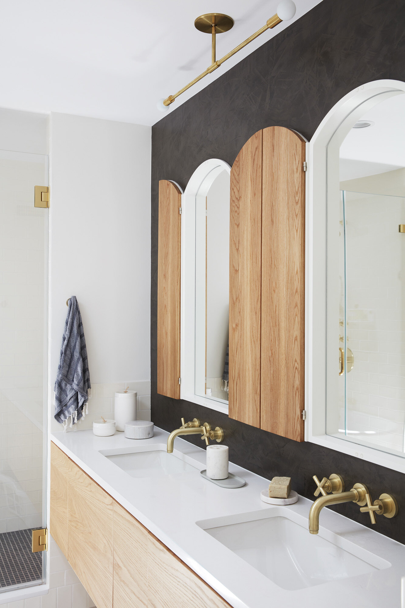 A dark accent wall contrasts with white finishes and light wood for a balanced, modern bathroom.