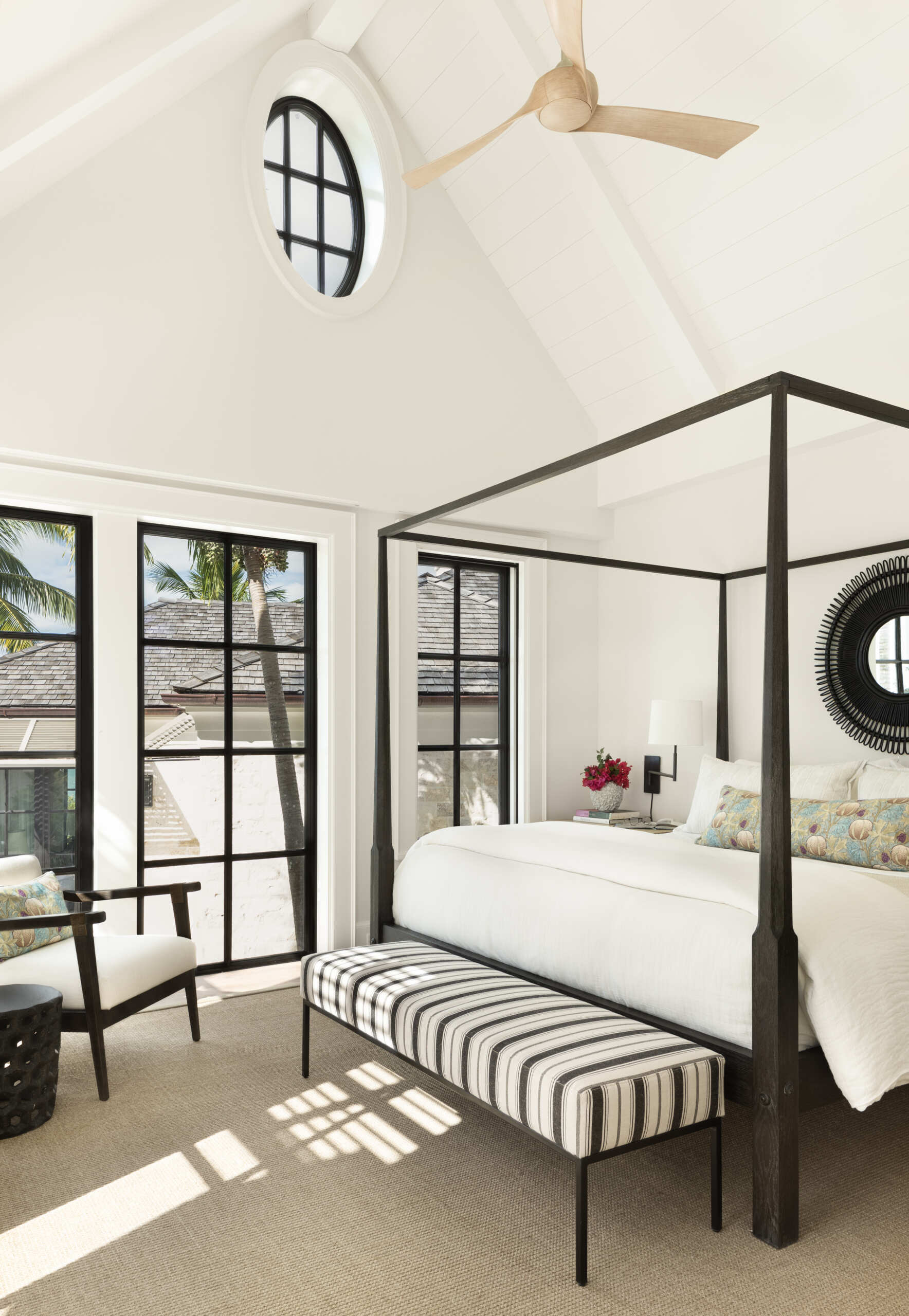 Calm island bedroom layered with soft whites, warm wood, and natural textures, where black framed doors and windows frame palm and ocean views like living artwork.