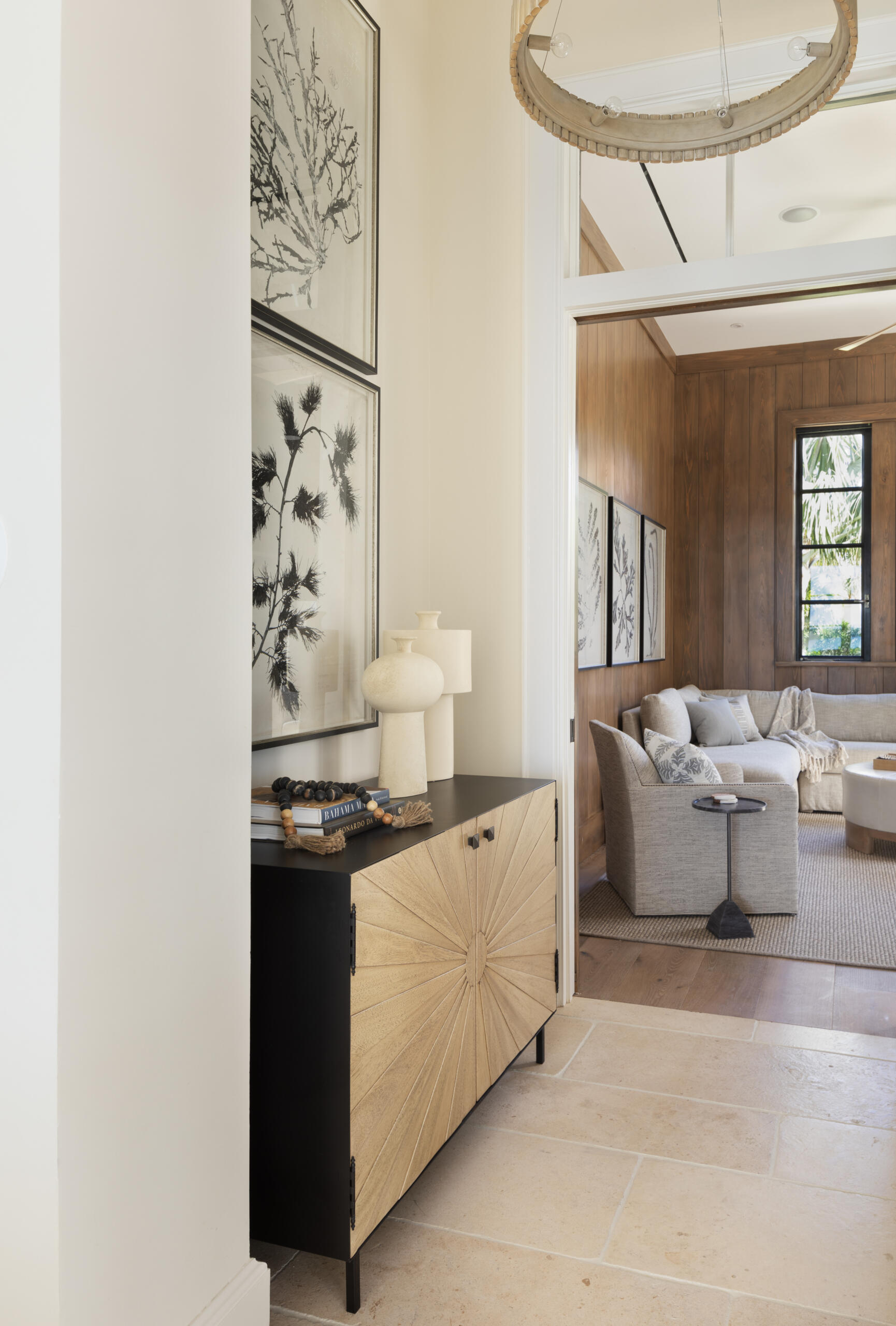 The entryway sets a calm, understated tone from the moment you arrive. Creamy walls and light stone floors reflect the natural light, keeping the space open and welcoming. A black and wood console introduces a subtle graphic note, while textured door fronts and framed botanicals add depth without visual noise. Sculptural accents and simple styling keep the mood relaxed, with warm wood details offering a quiet preview of the living spaces beyond.