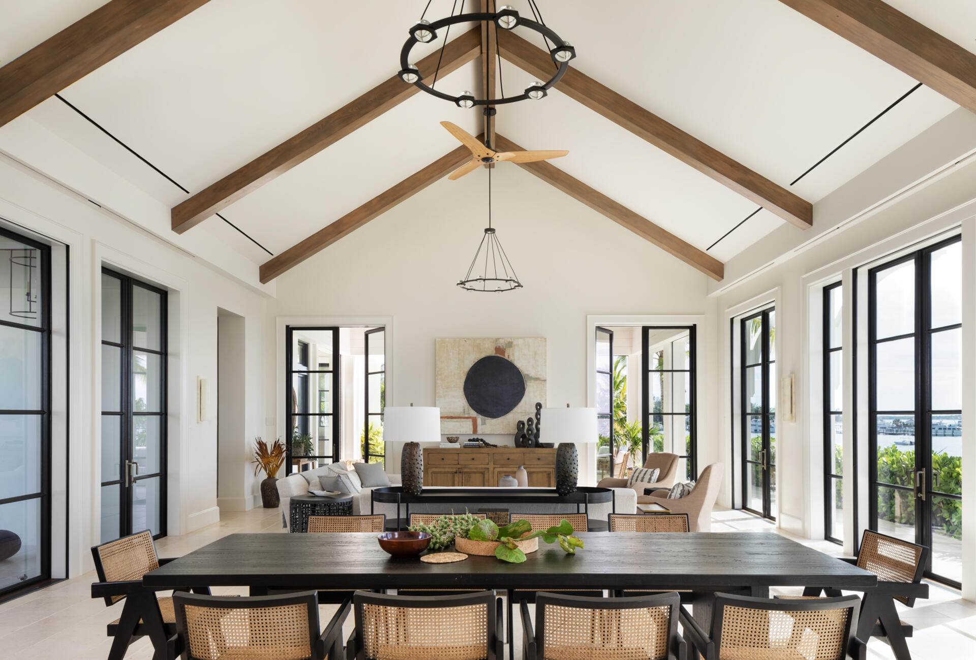 Living room with soaring pitched ceilings, exposed timber beams, and black framed doors that open the space to light and island views. A relaxed layout that balances scale with softness.