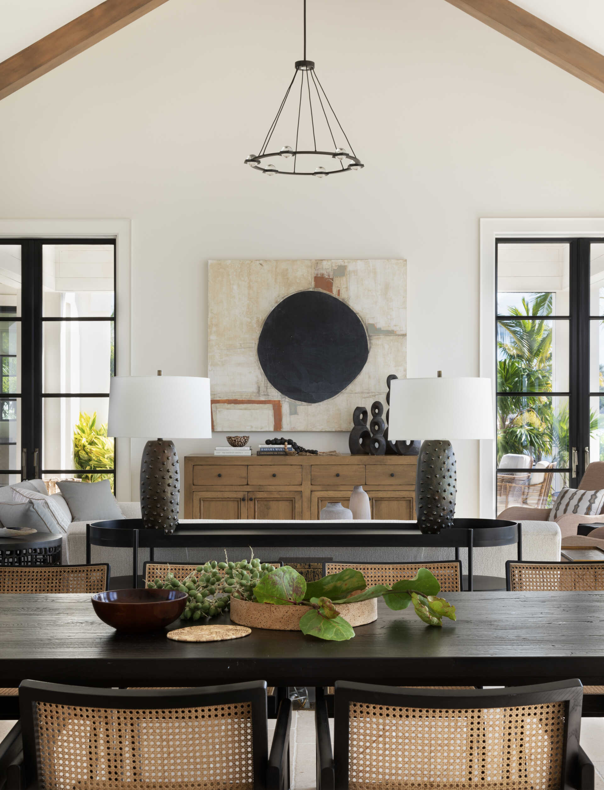 Living room with soaring pitched ceilings, exposed timber beams, and black framed doors that open the space to light and island views. A relaxed layout that balances scale with softness.