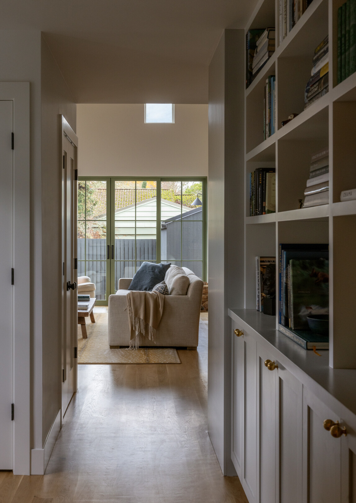 El pasillo parece una pasarela tranquila, con una suave luz natural que ilumina los pisos de madera clara y los estantes y gabinetes empotrados.