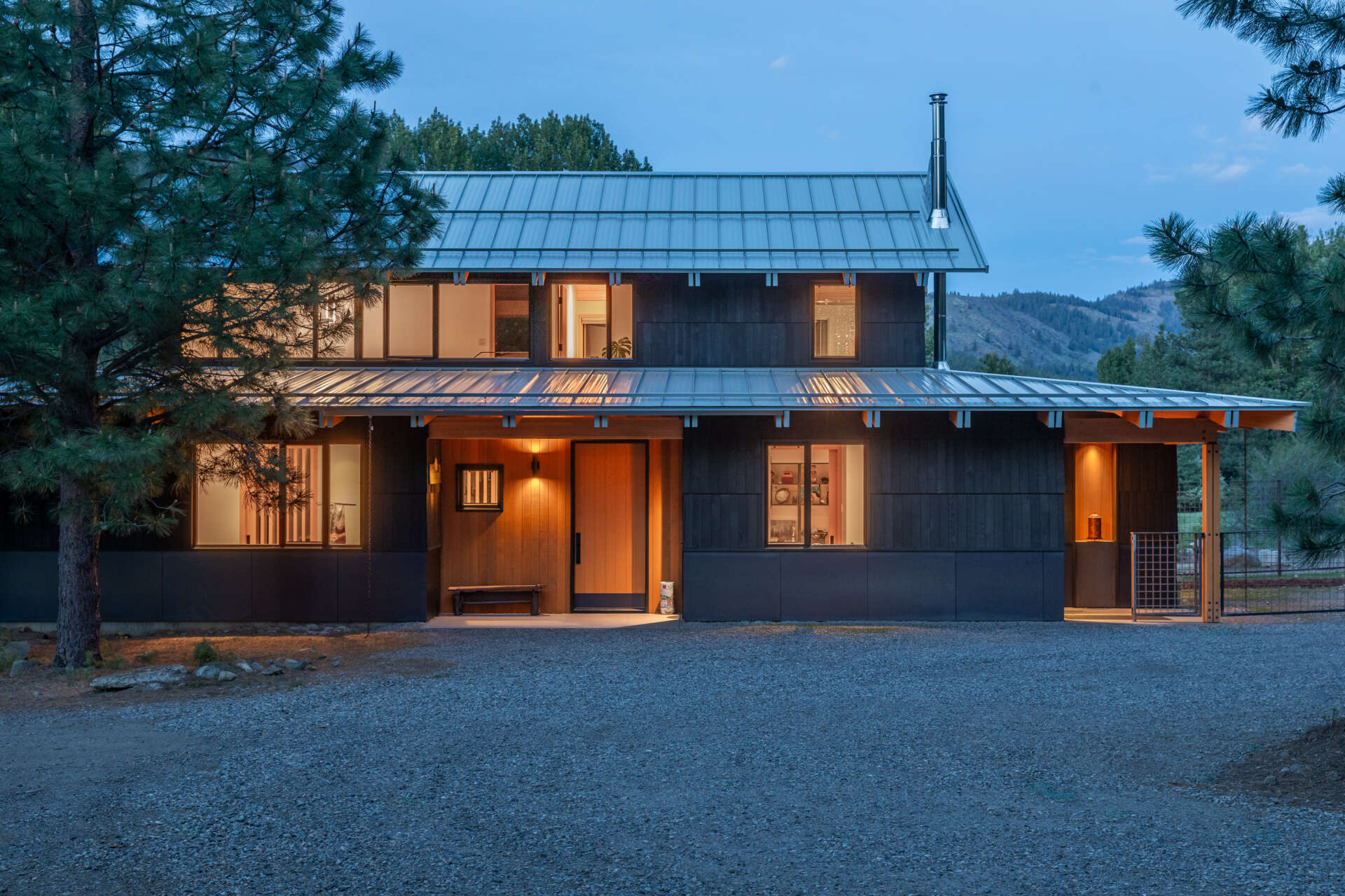 Charcoal wood siding, warm timber accents, and a simple gravel approach create a welcoming arrival that feels grounded in the surrounding mountain landscape.