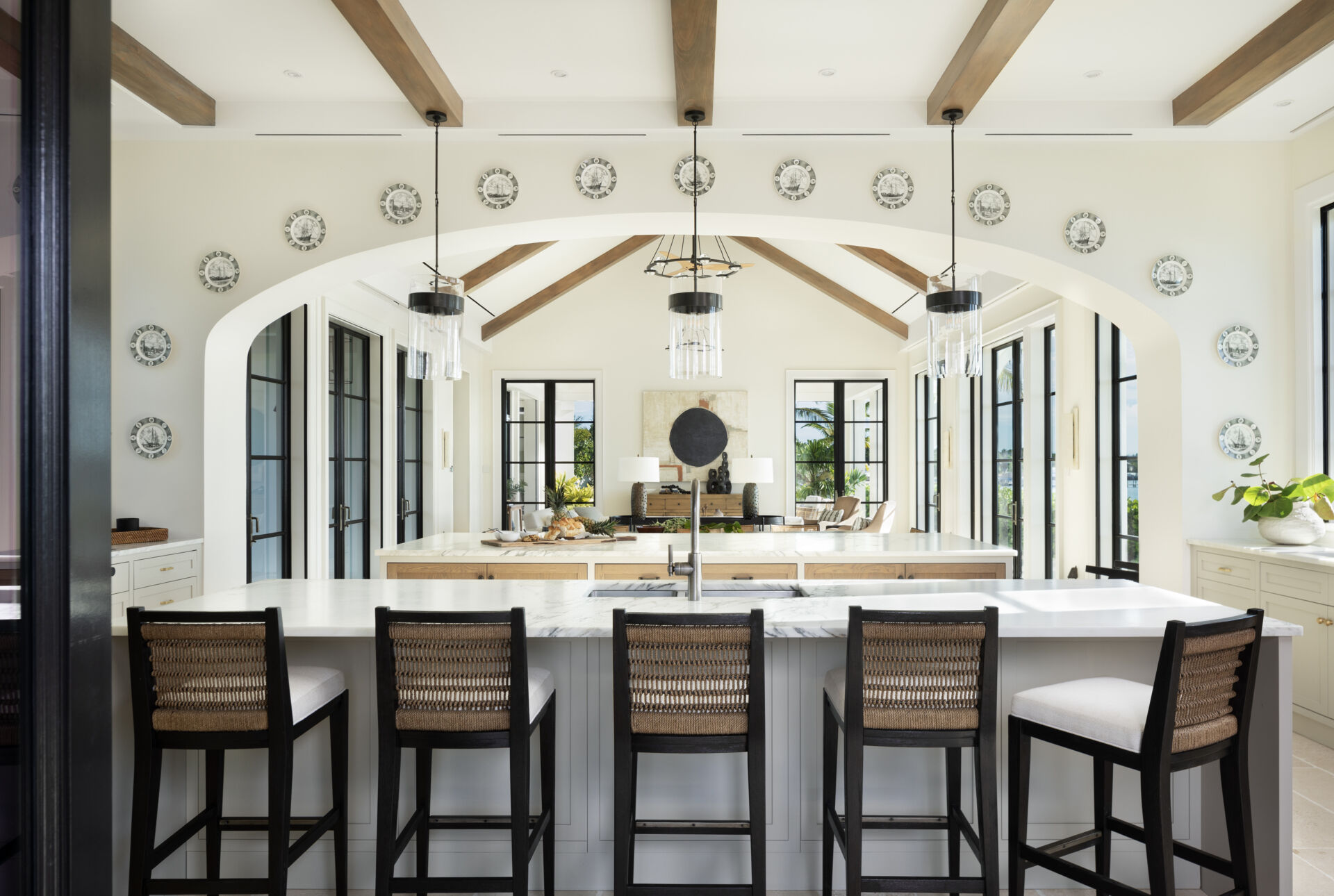 Bright Caribbean kitchen with dual islands, designed as the heart of the home, with pale cabinetry, timber ceiling beams, and large black framed windows that turn everyday moments into view-focused rituals.