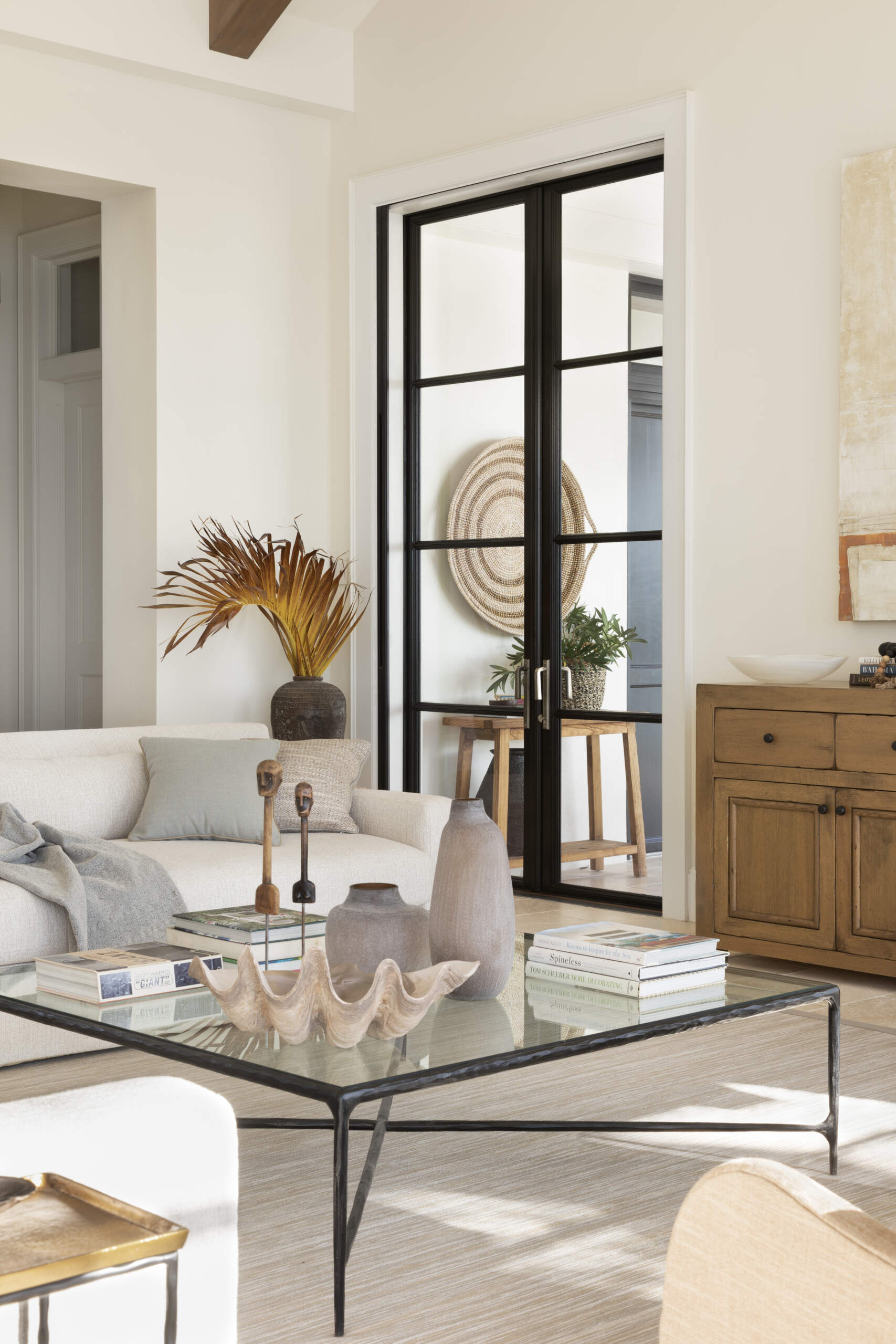 Living room with soaring pitched ceilings, exposed timber beams, and black framed doors that open the space to light and island views. A relaxed layout that balances scale with softness.
