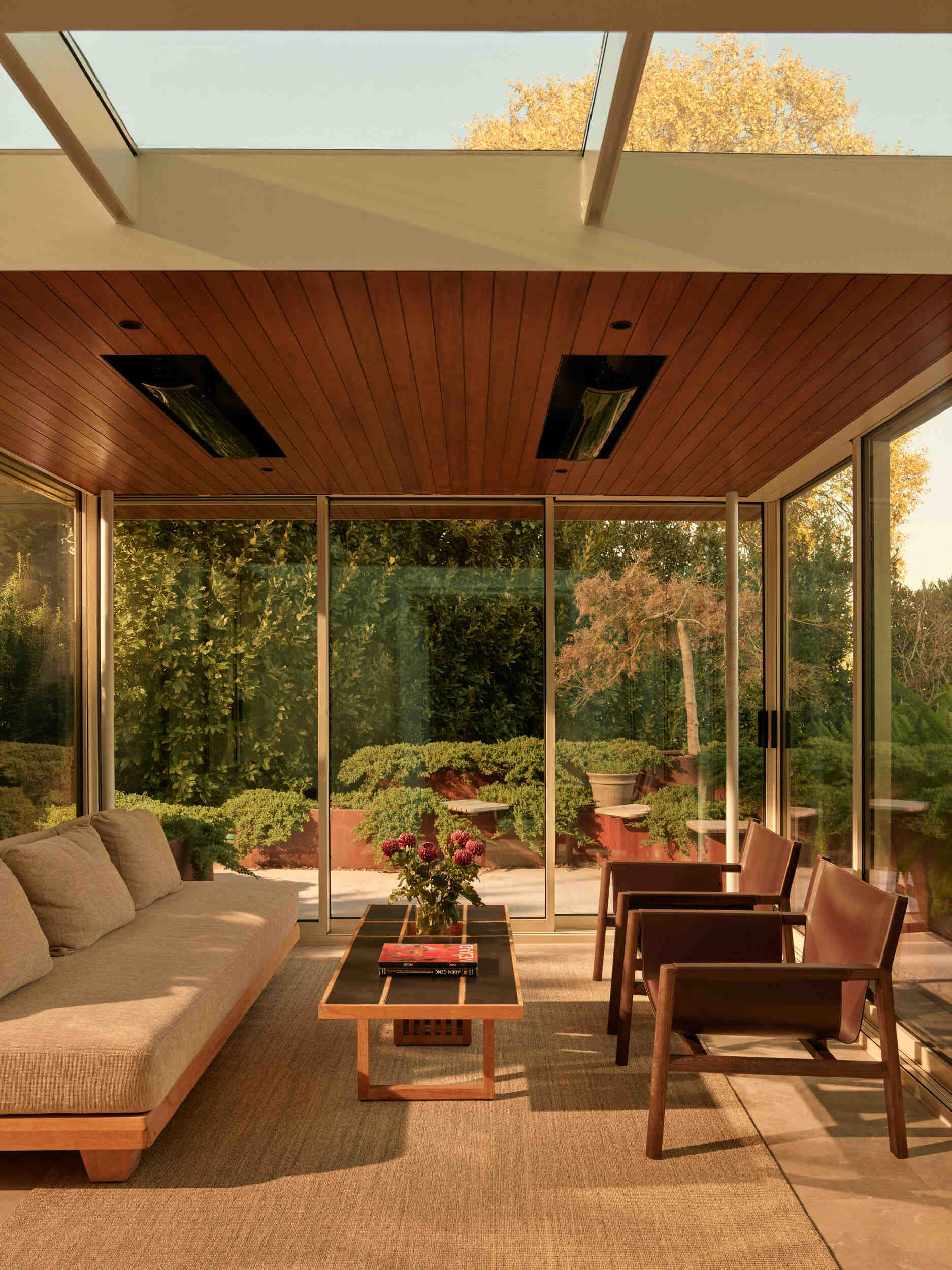 The sunroom is a calm in-between space, part living room, part garden lounge. Floor-to-ceiling glass surrounds the area, while a warm wood ceiling adds a cozy touch. A linen-toned sofa and simple wood chairs keep the room relaxed. Skylights overhead make it perfect for morning coffee or golden-hour unwinding.