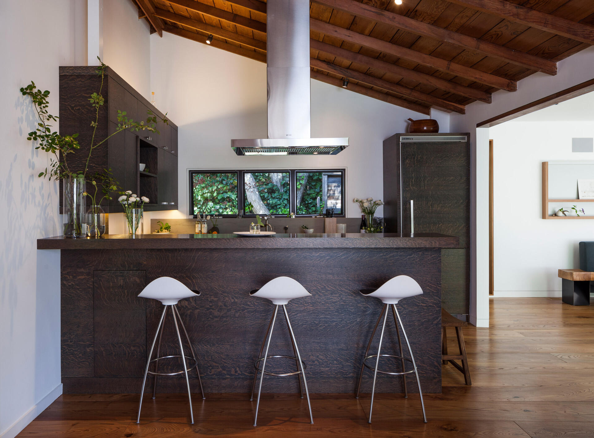 A galley-style kitchen connects to the dining area, featuring views of the fireplace and surrounding trees.