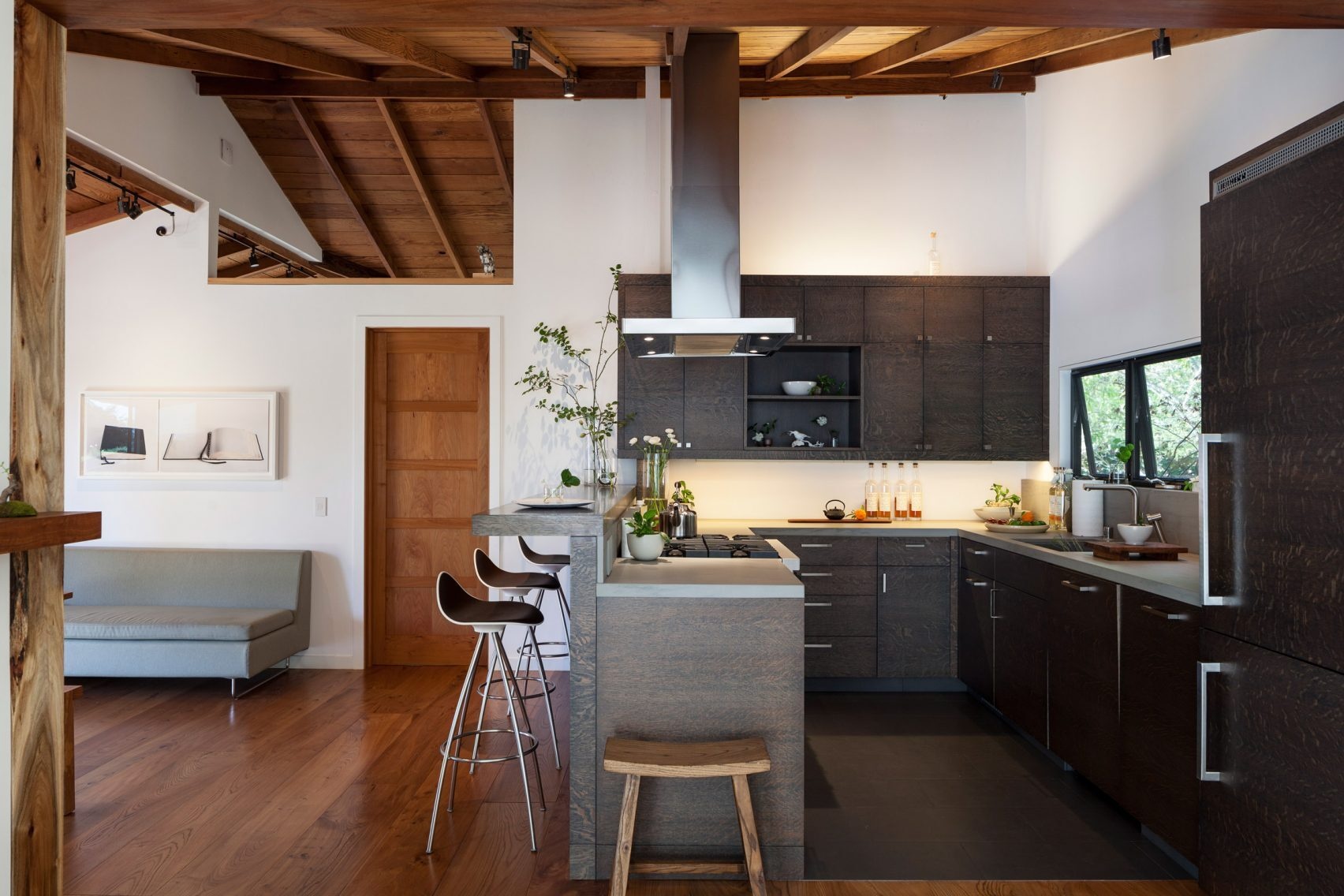 A galley-style kitchen connects to the dining area, featuring views of the fireplace and surrounding trees.