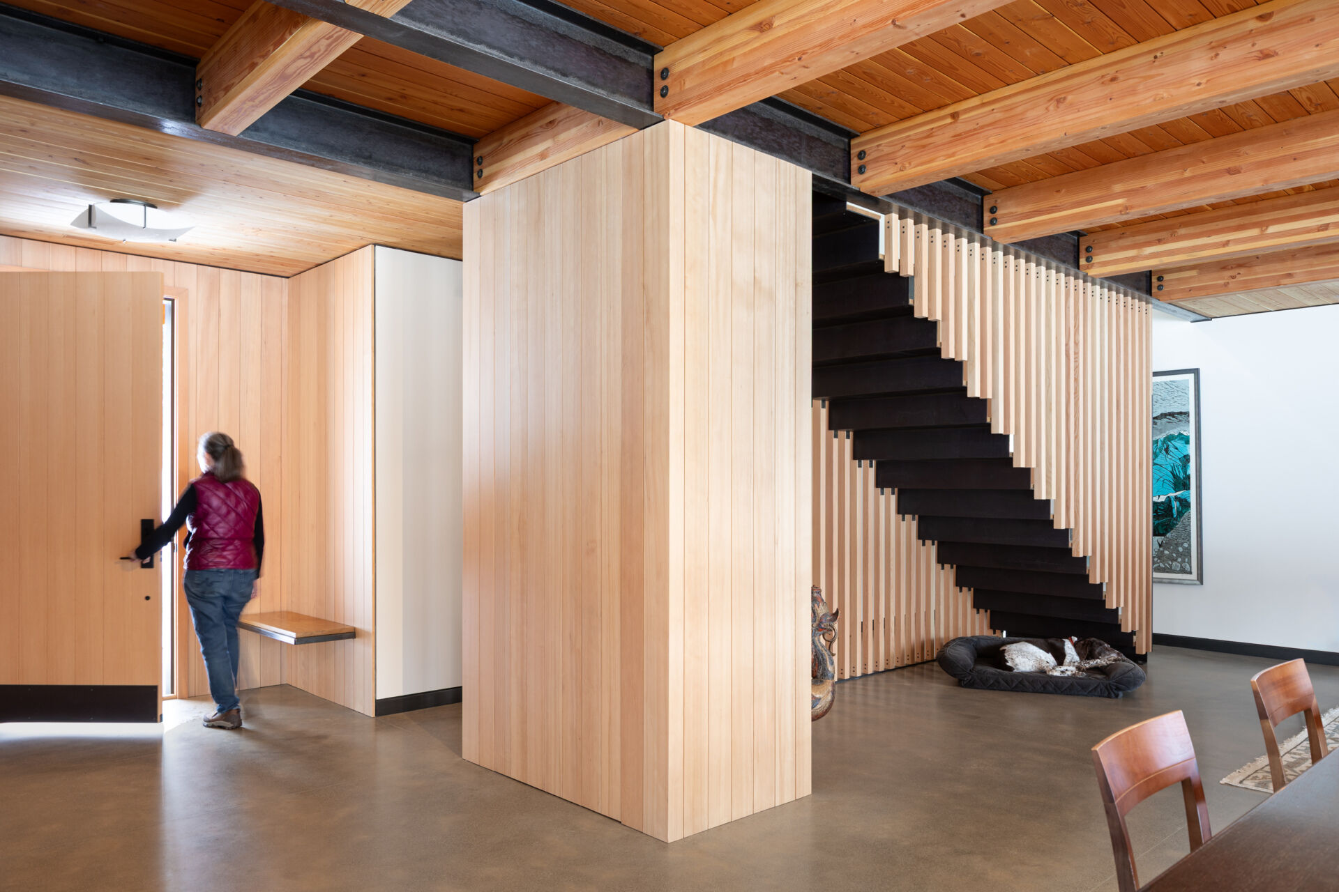 A calm, functional entryway defined by pale wood walls, black steel details, and polished concrete floors, designed to handle daily life with ease and intention.