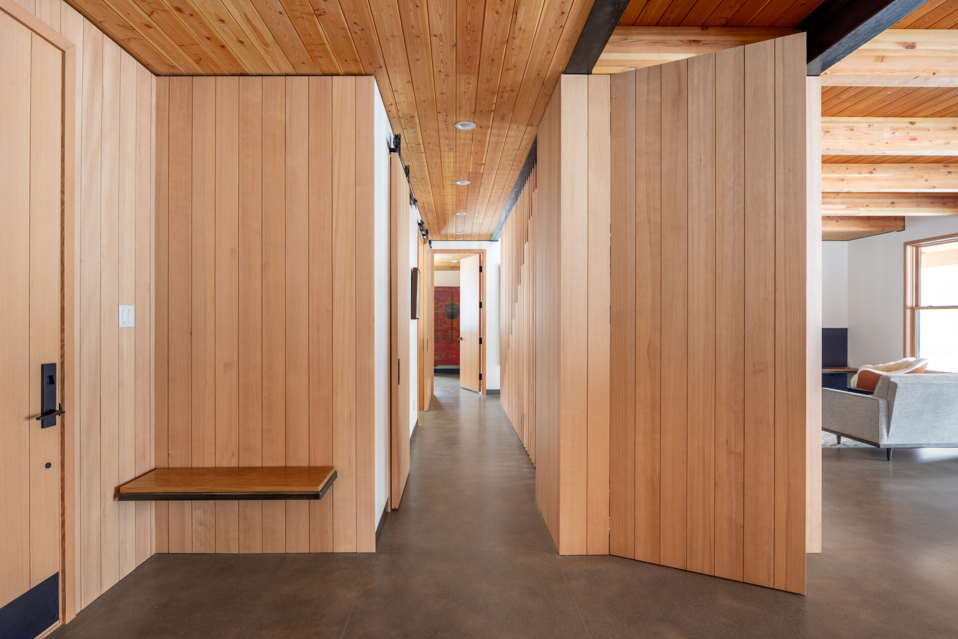 A calm, functional entryway defined by pale wood walls, black steel details, and polished concrete floors, designed to handle daily life with ease and intention.
