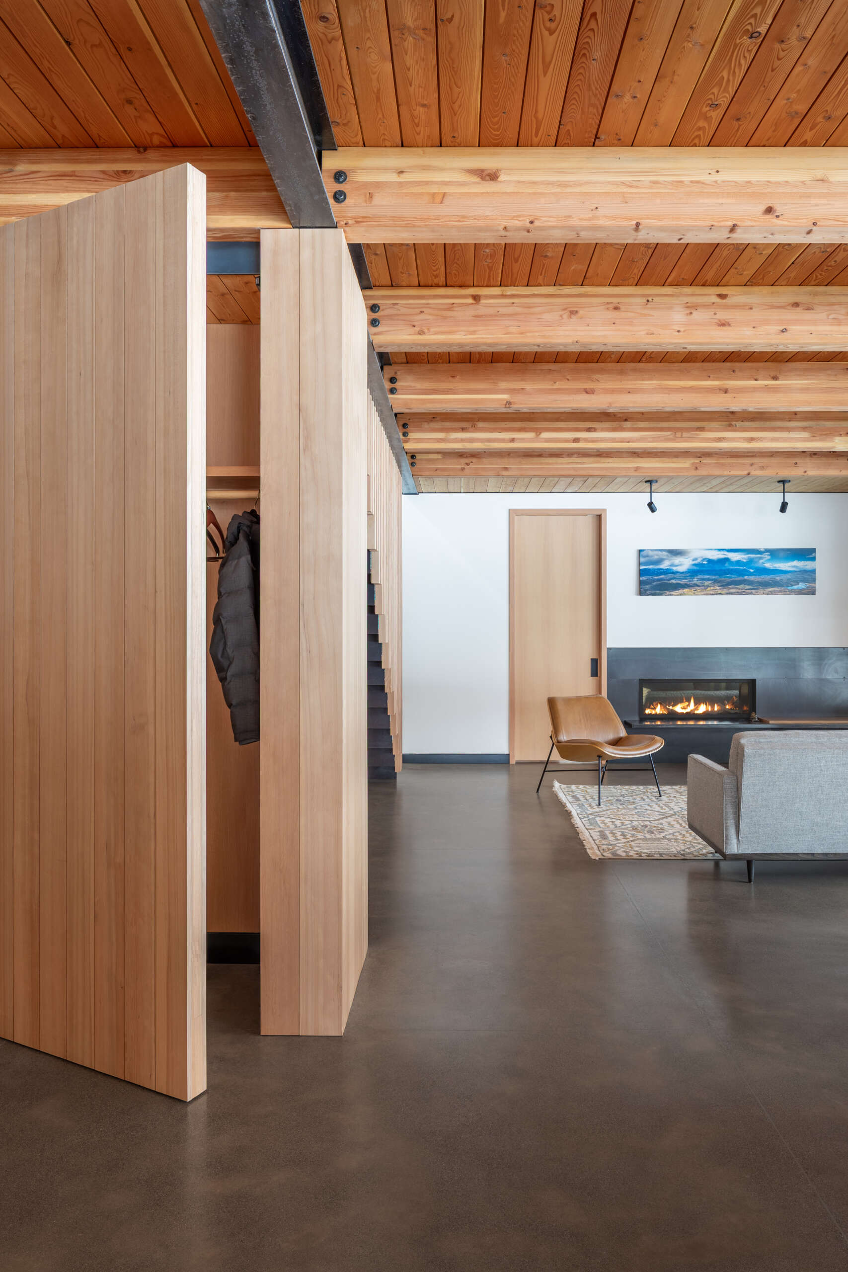 A calm, functional entryway defined by pale wood walls, black steel details, and polished concrete floors, designed to handle daily life with ease and intention.