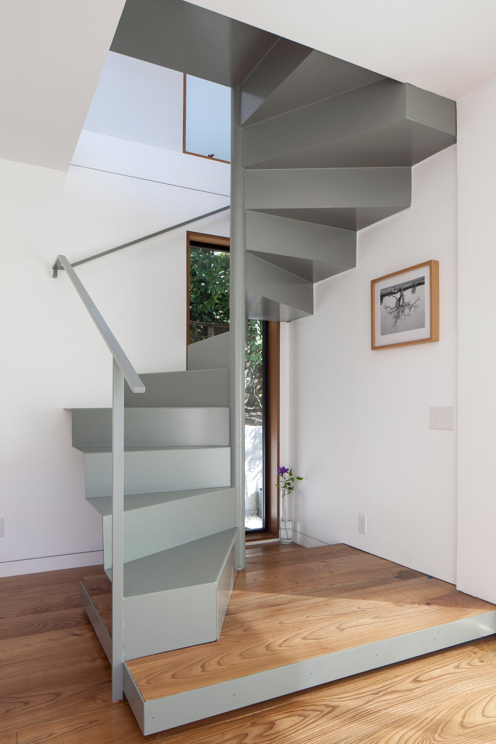 A sleek grey steel staircase provides access to the upper floor while keeping the design minimal and modern.