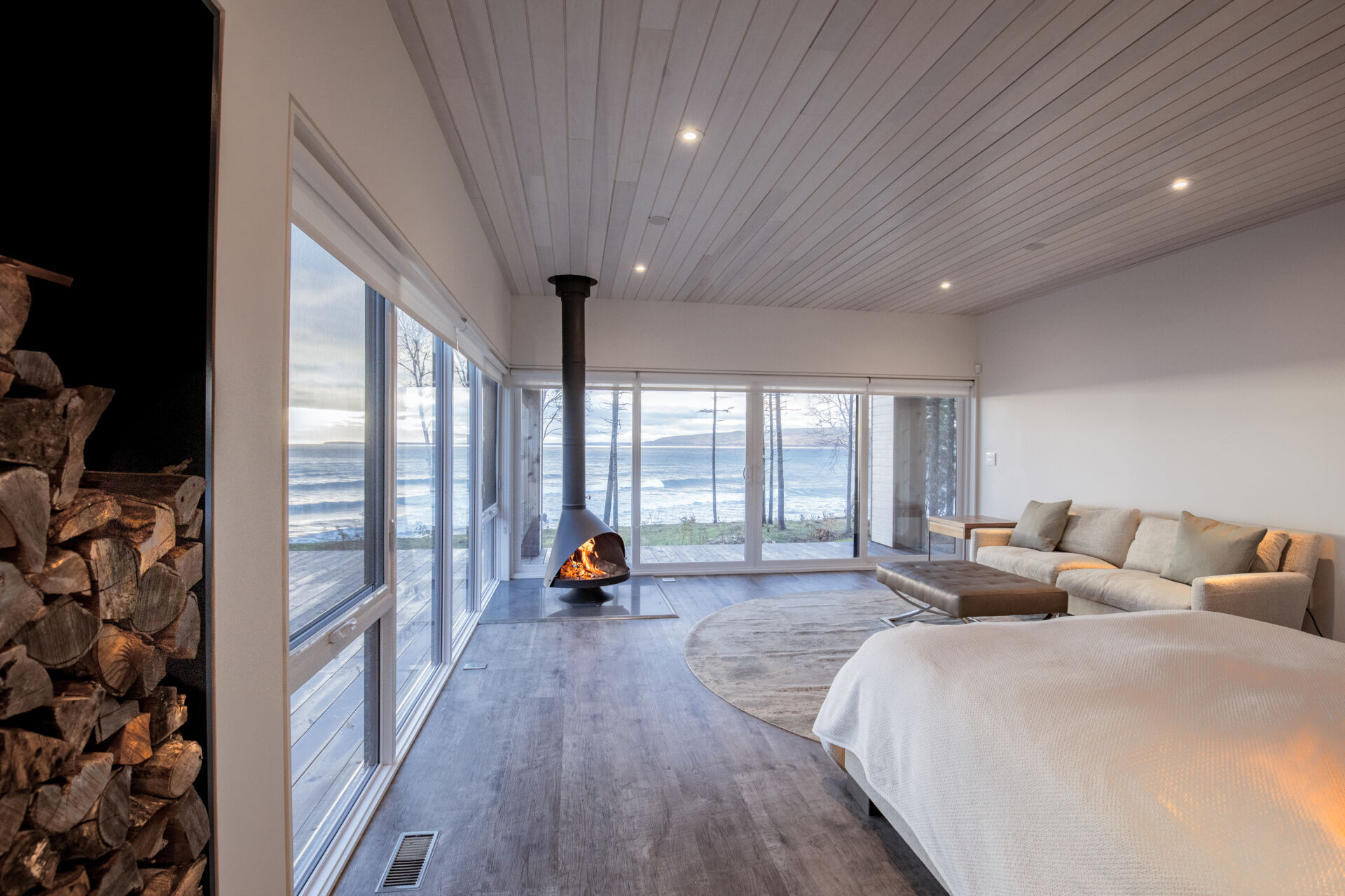 La cabaña cuenta con una pared de ventanas y una chimenea de leña.
