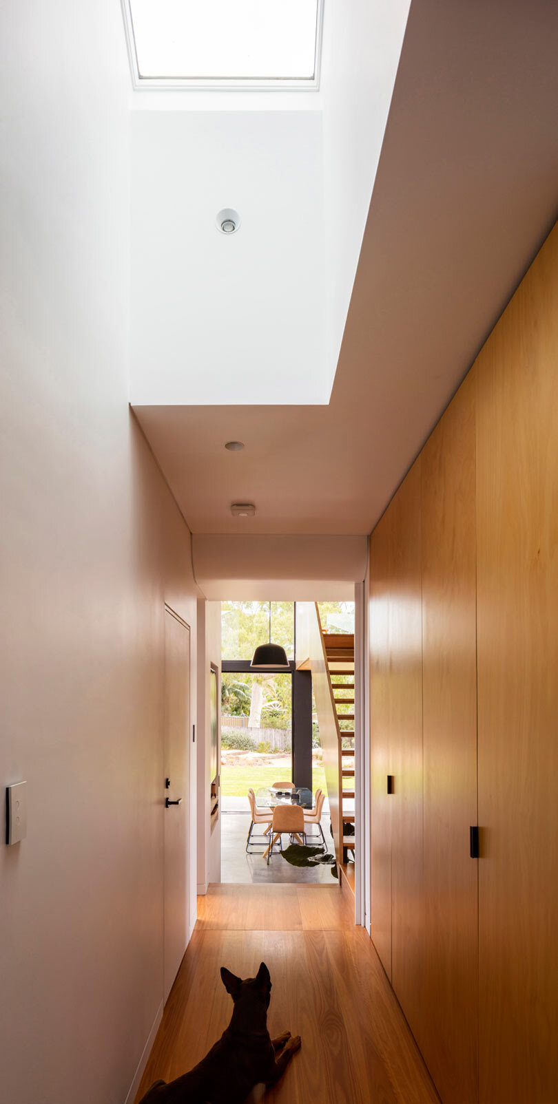 A skylit hallway with warm timber storage creates a calm transition between the original 1960s home and the modern rear extension.