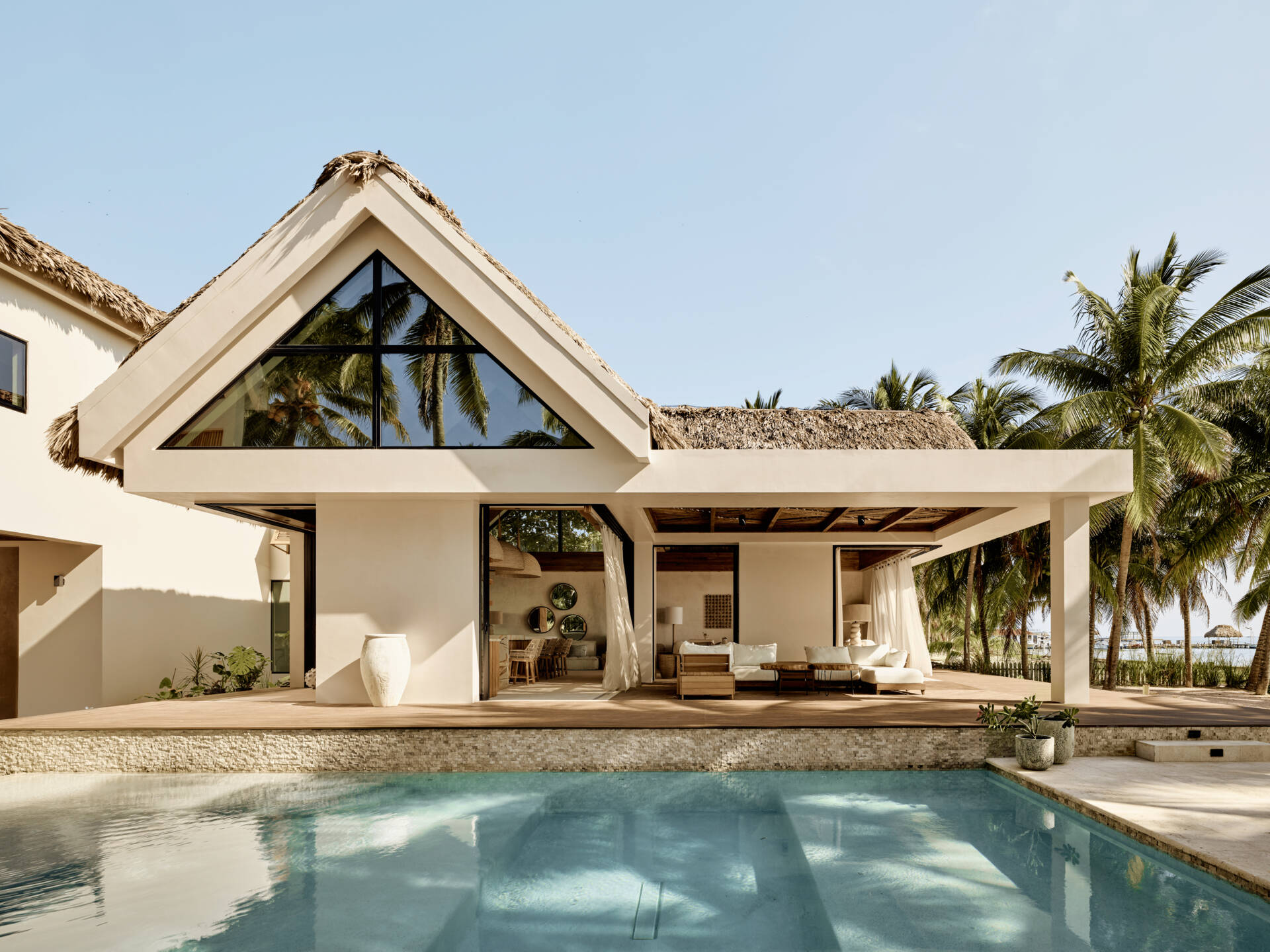 The pool anchors the main living areas and acts as a visual and social connector between the structures. It sits just beyond the living room, reinforcing the idea that outdoor spaces are part of everyday life. Movement between swimming, dining, and lounging happens without separation, keeping everyone within view.