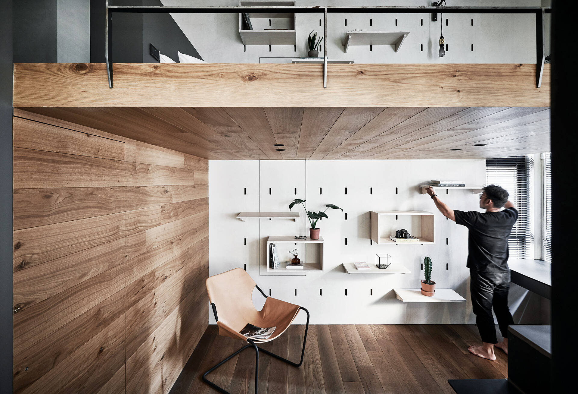 A home office in a compact apartment features adjustable pegboard shelving and hidden storage to maintain a clean, functional layout.
